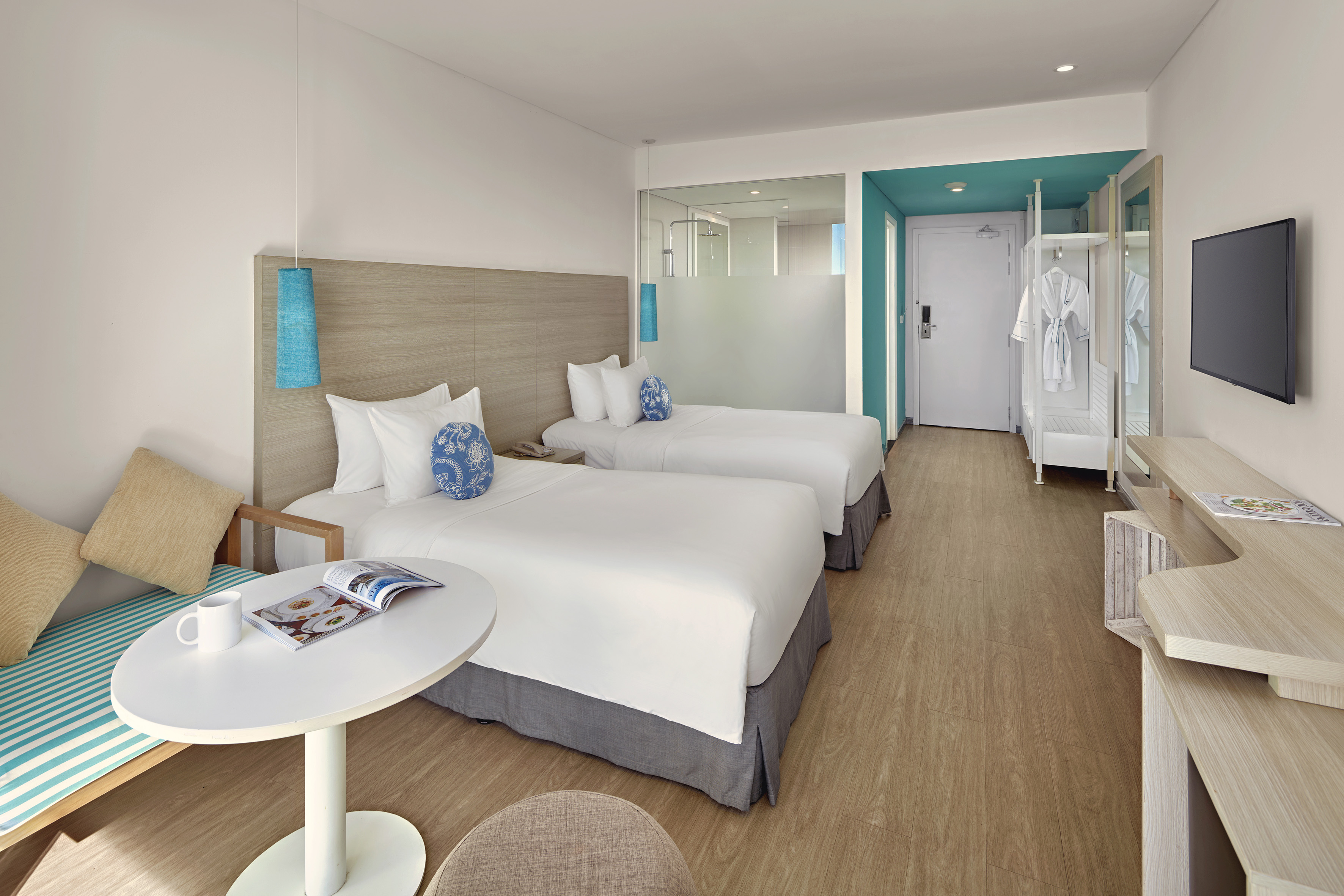 Bright, modern hotel room with two twin beds and teal design elements.