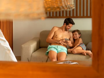 a man and child sitting on a couch looking at a cellphone