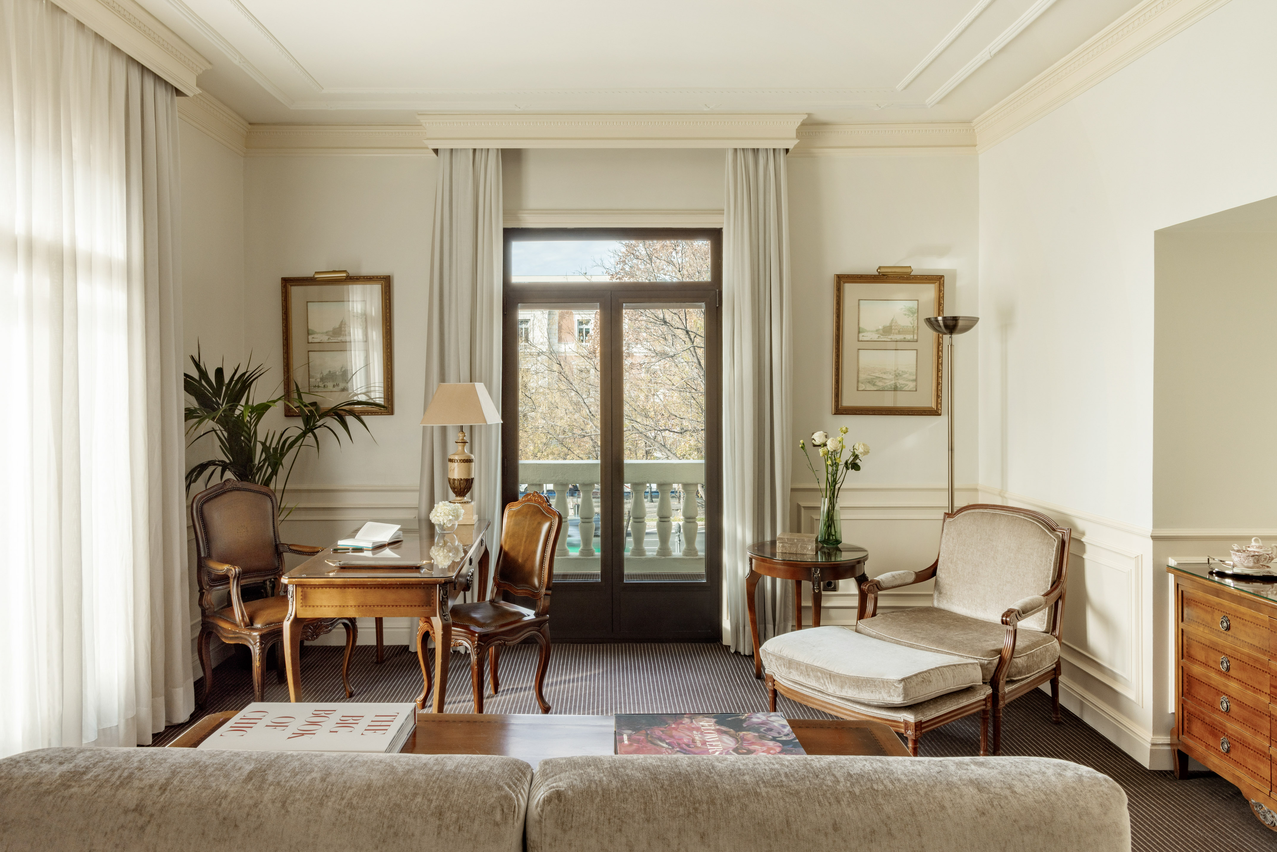 Elegant hotel suite living room with desk, armchair, and balcony view.