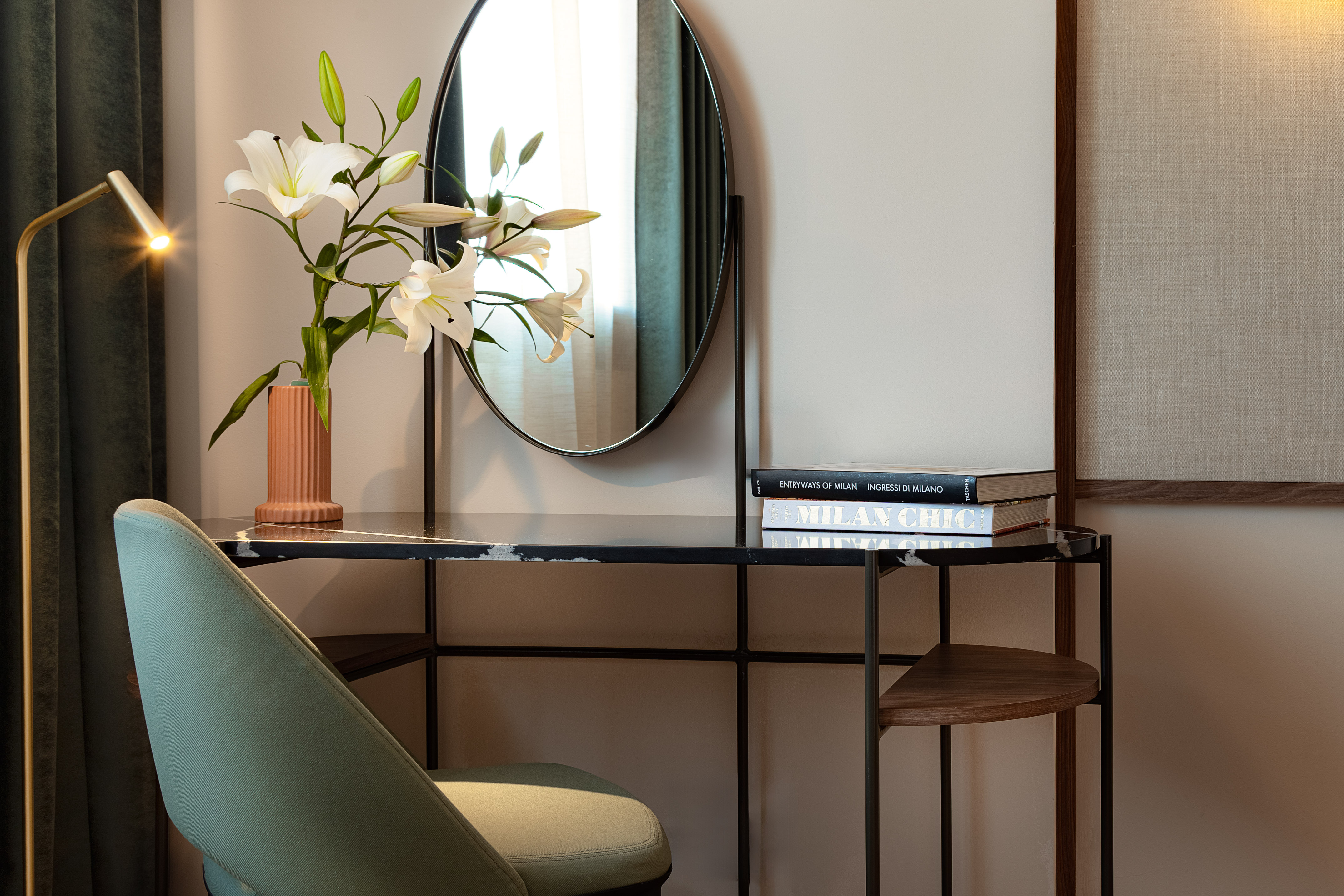 Modern vanity with round mirror, white lilies, lamp, and design books.