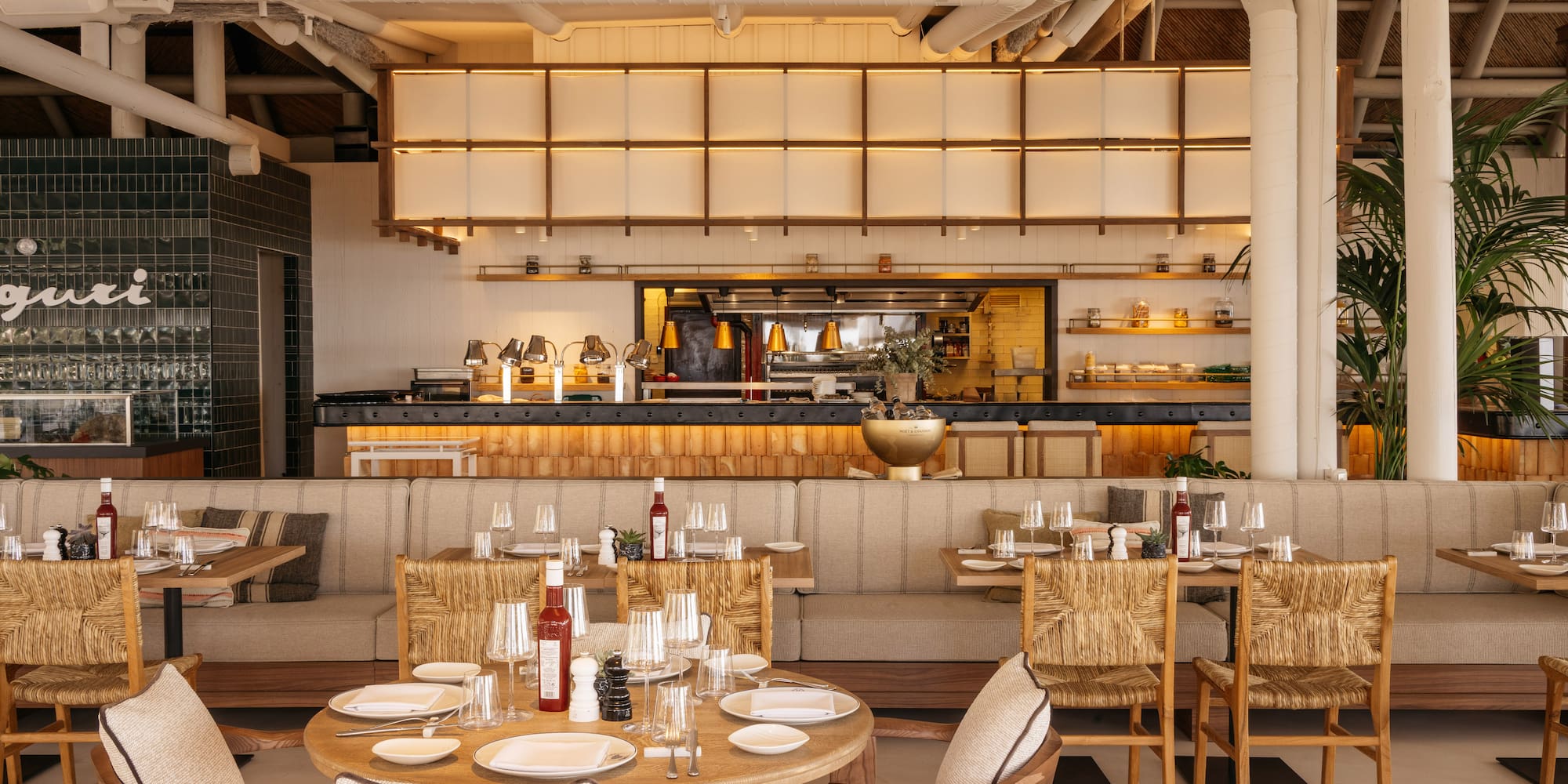 Elegant restaurant interior with set tables, open kitchen, and natural decor.