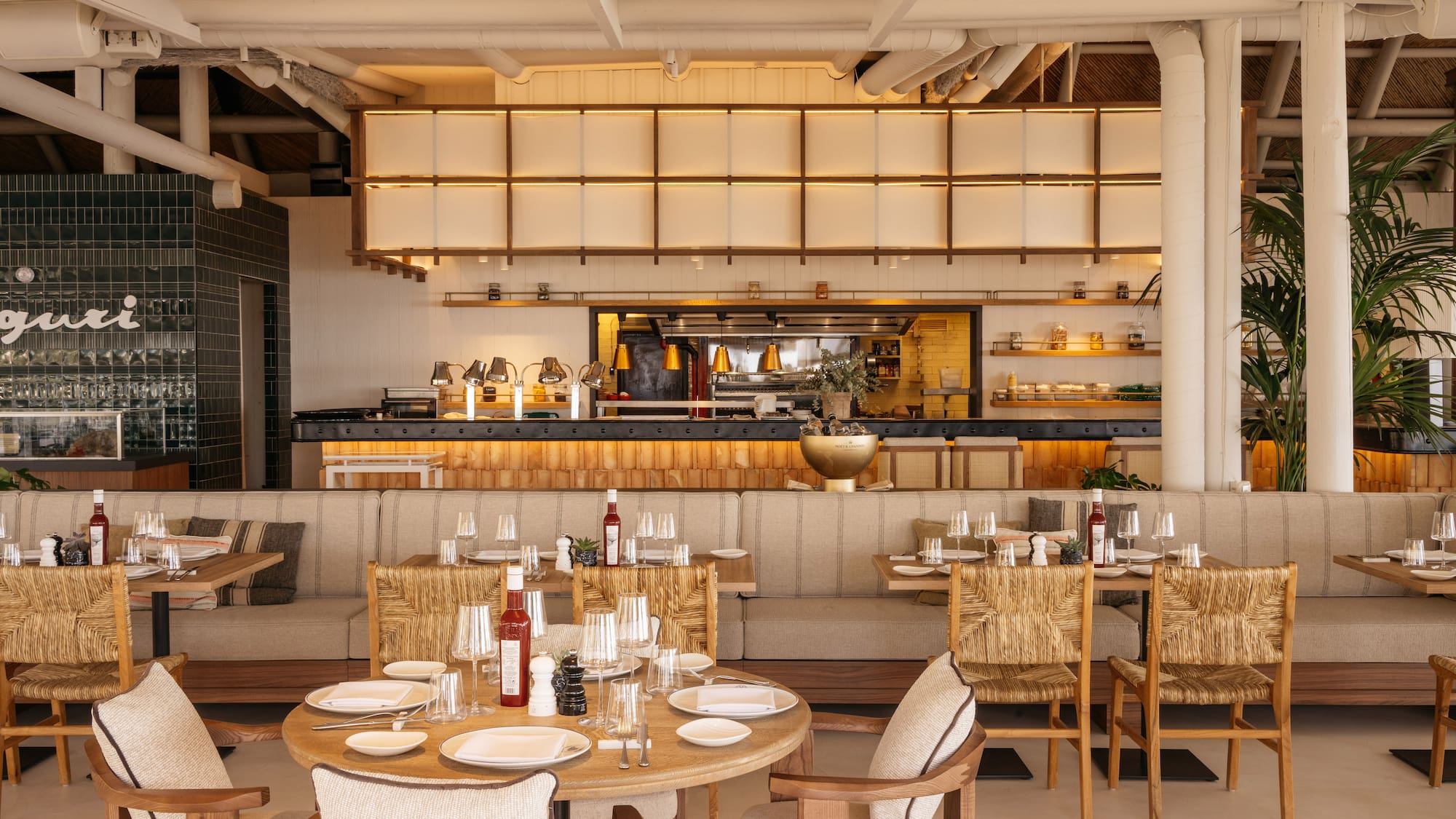 Elegant restaurant interior with set tables, open kitchen, and natural decor.