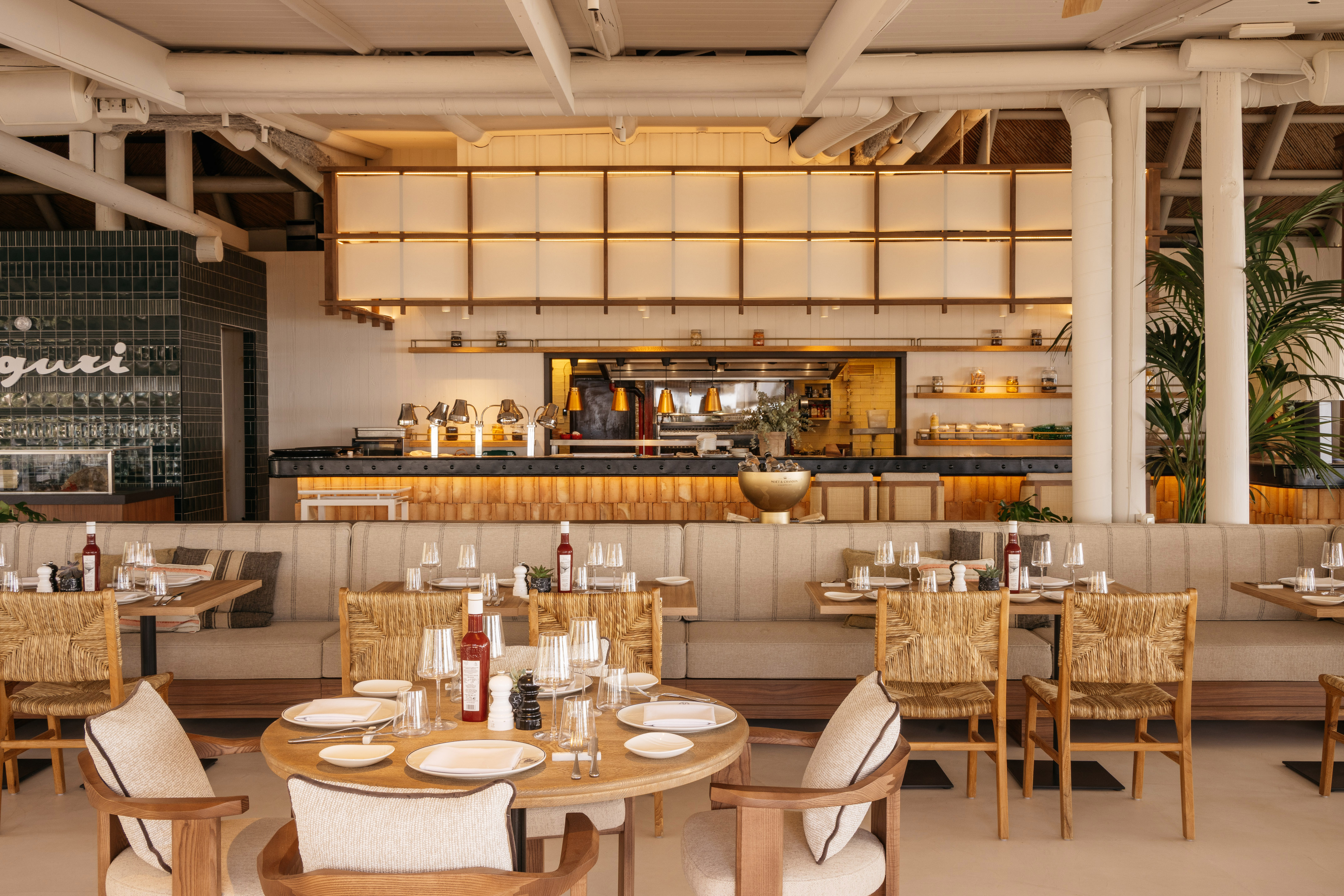 Elegant restaurant interior with set tables, open kitchen, and natural decor.