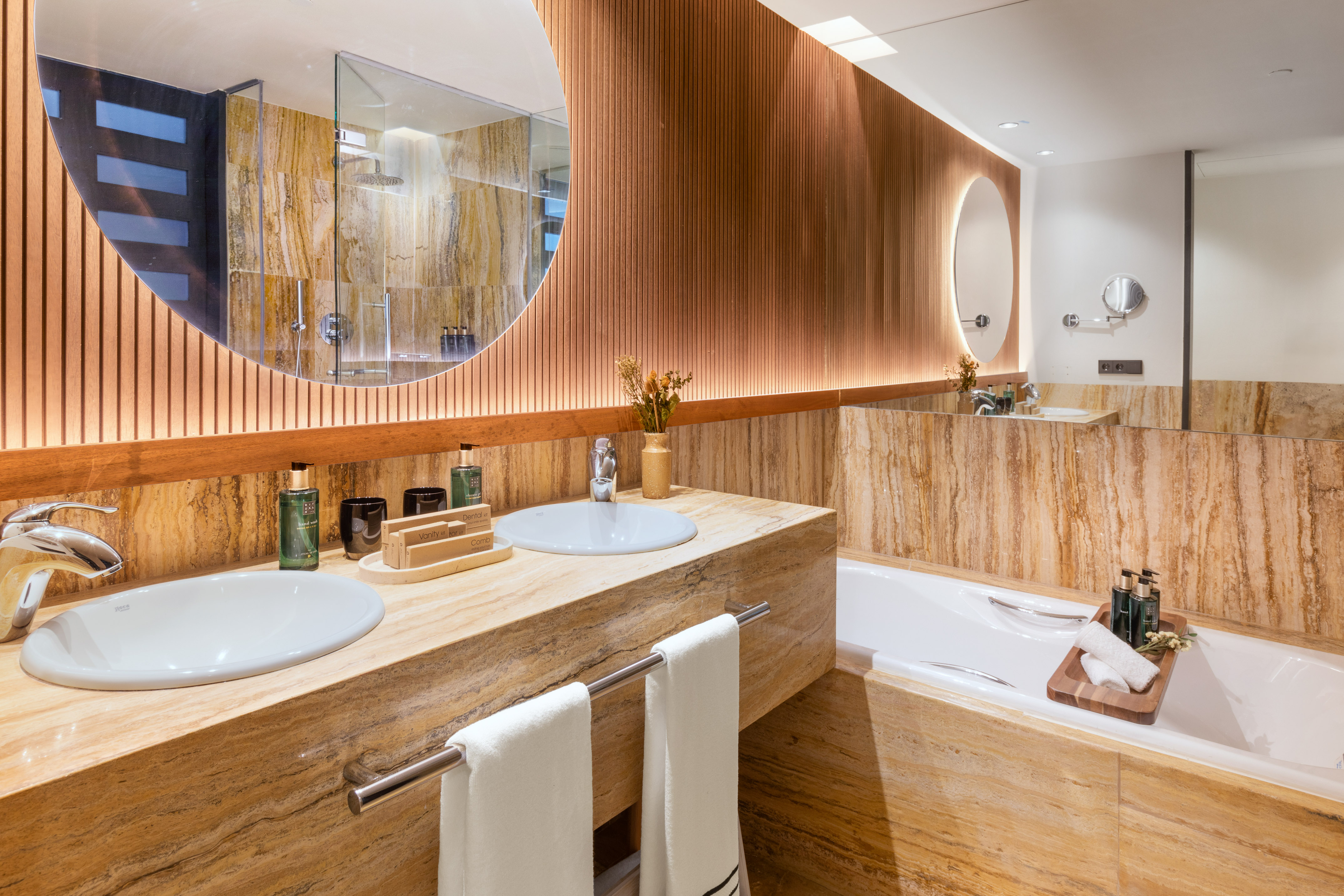 Luxury bathroom: marble double vanity, wood panels, round mirror, bathtub.