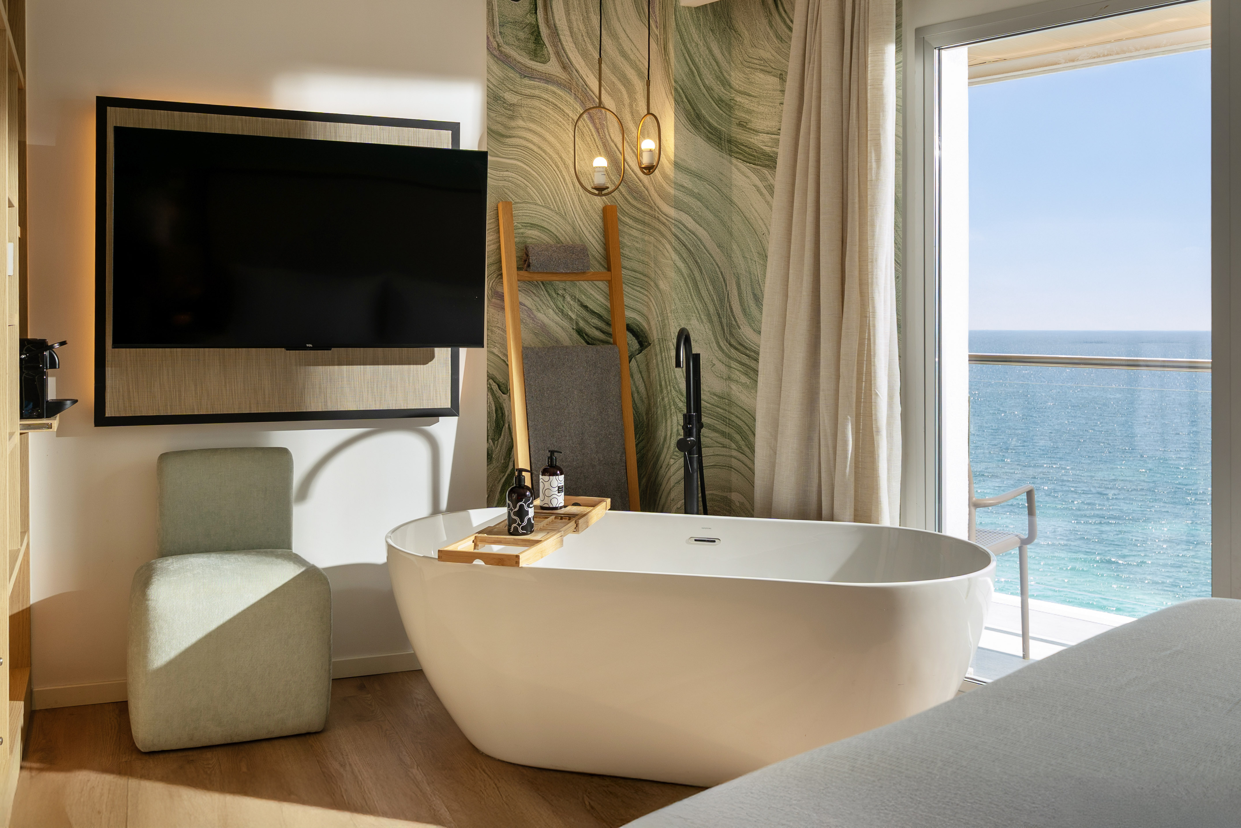 Ocean view hotel room with freestanding bathtub, TV, and contemporary design.