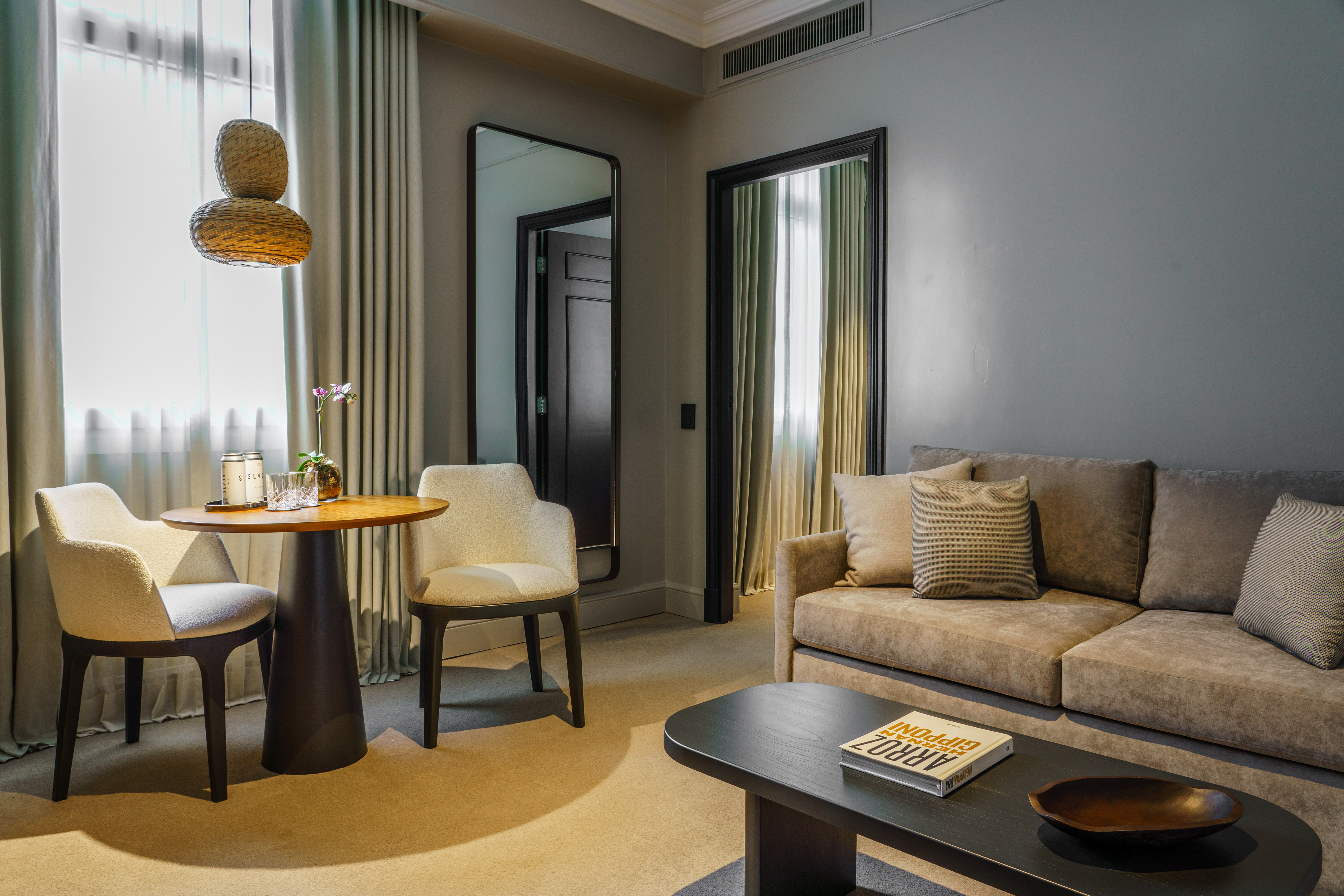 Modern hotel suite living space with sofa, dining table, and woven light.