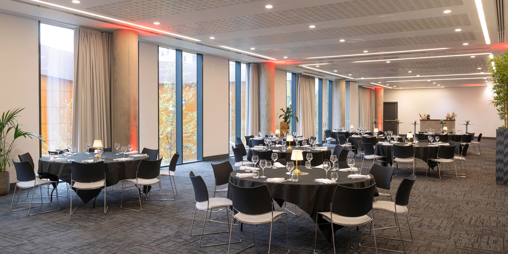 Spacious event room with black tables, large windows, and red accent lighting.