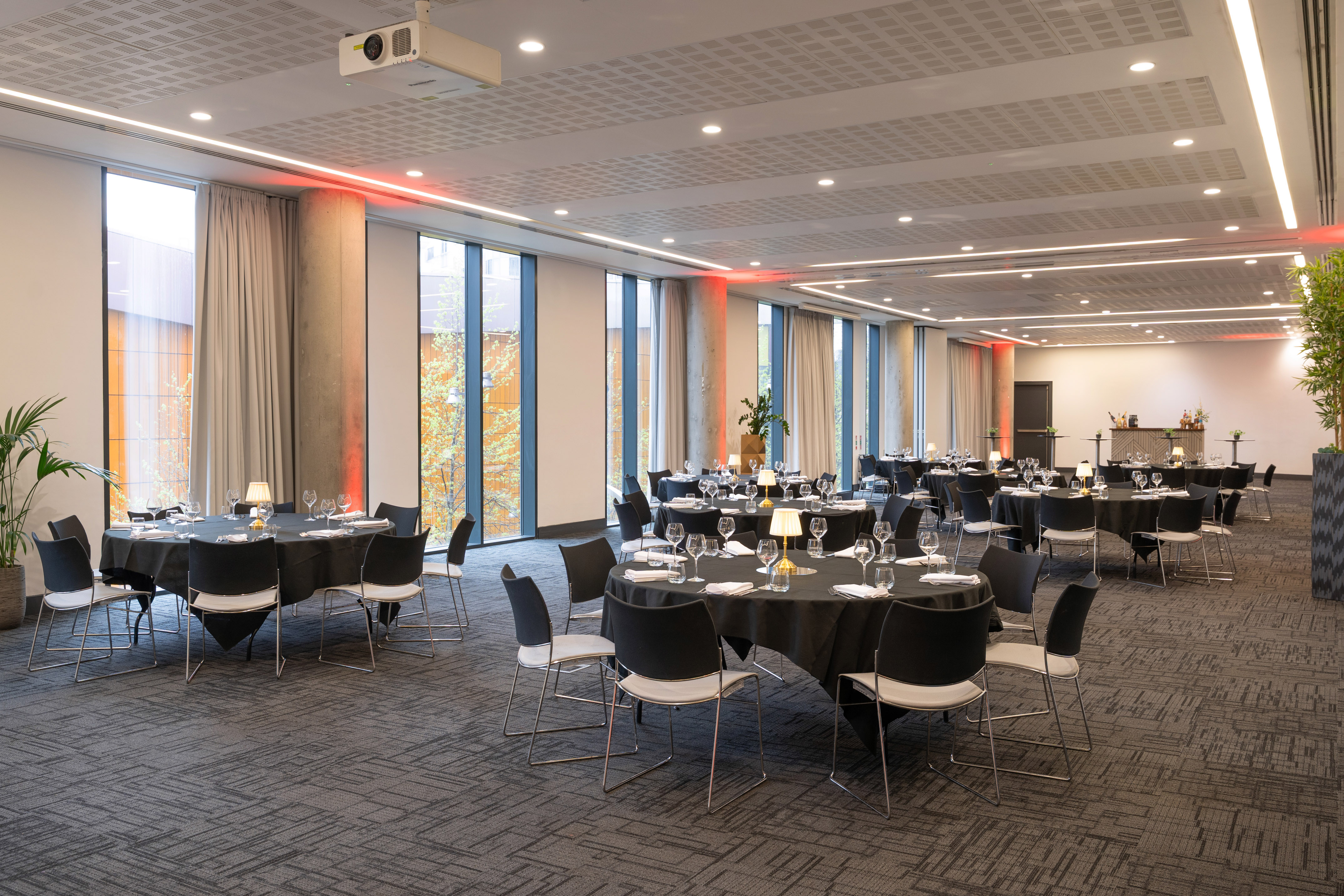 Spacious event room with black tables, large windows, and red accent lighting.