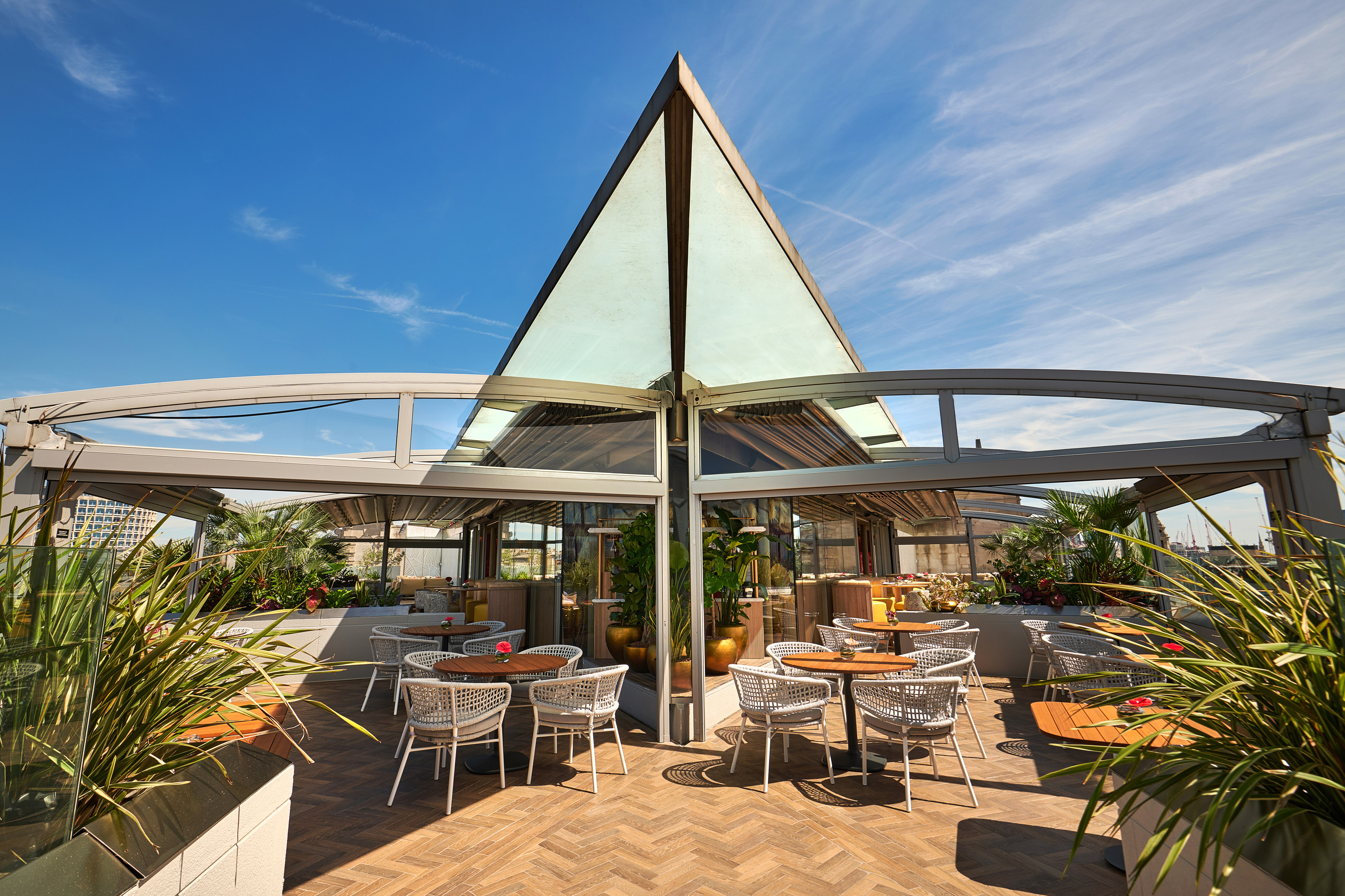 Stylish outdoor restaurant terrace with glass roof, modern tables, and plants.