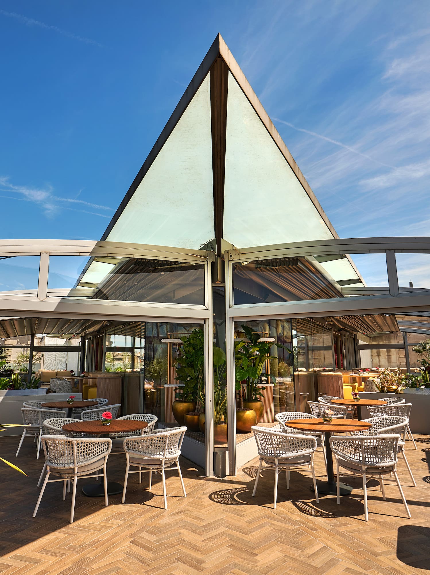 Stylish outdoor restaurant terrace with glass roof, modern tables, and plants.