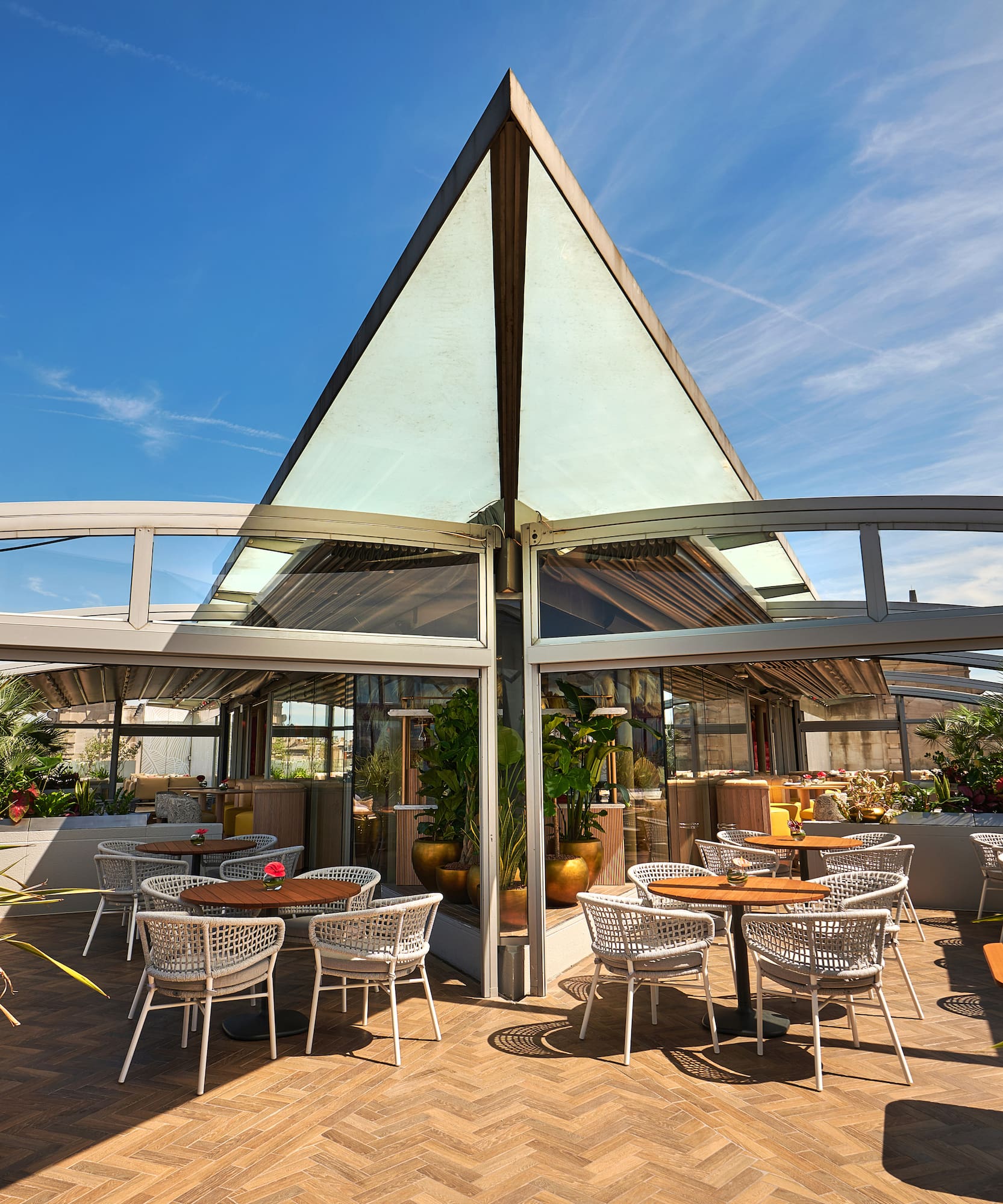 Stylish outdoor restaurant terrace with glass roof, modern tables, and plants.