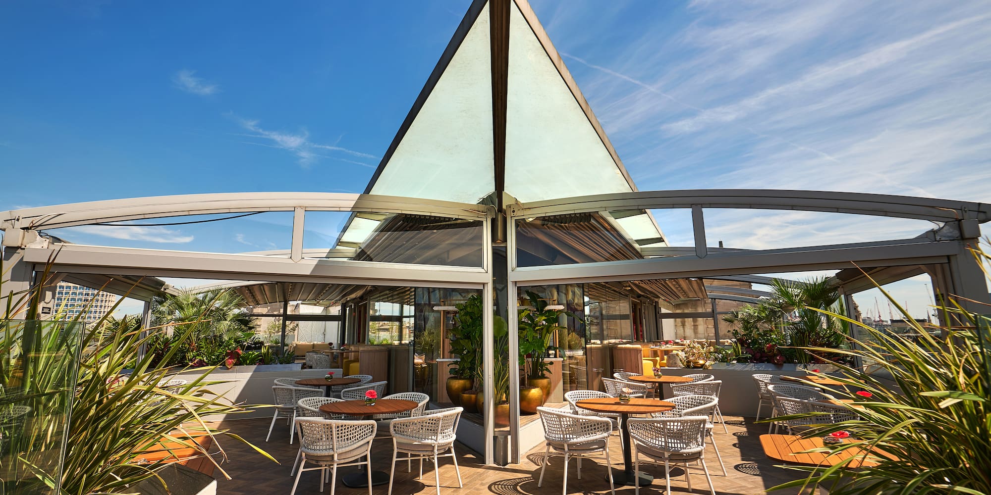 Stylish outdoor restaurant terrace with glass roof, modern tables, and plants.