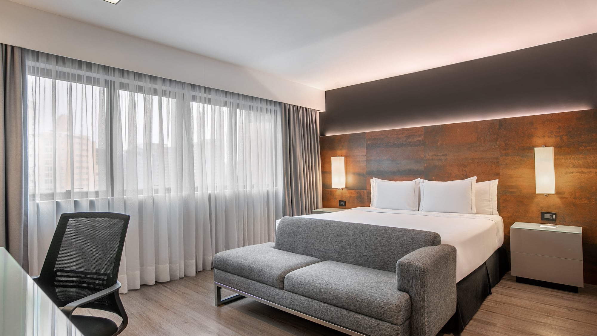 Quarto de hotel moderno com cama de casal, sofá cinza e escrivaninha. - Deluxe Room Queen - Meliá Ibirapuera, São Paulo