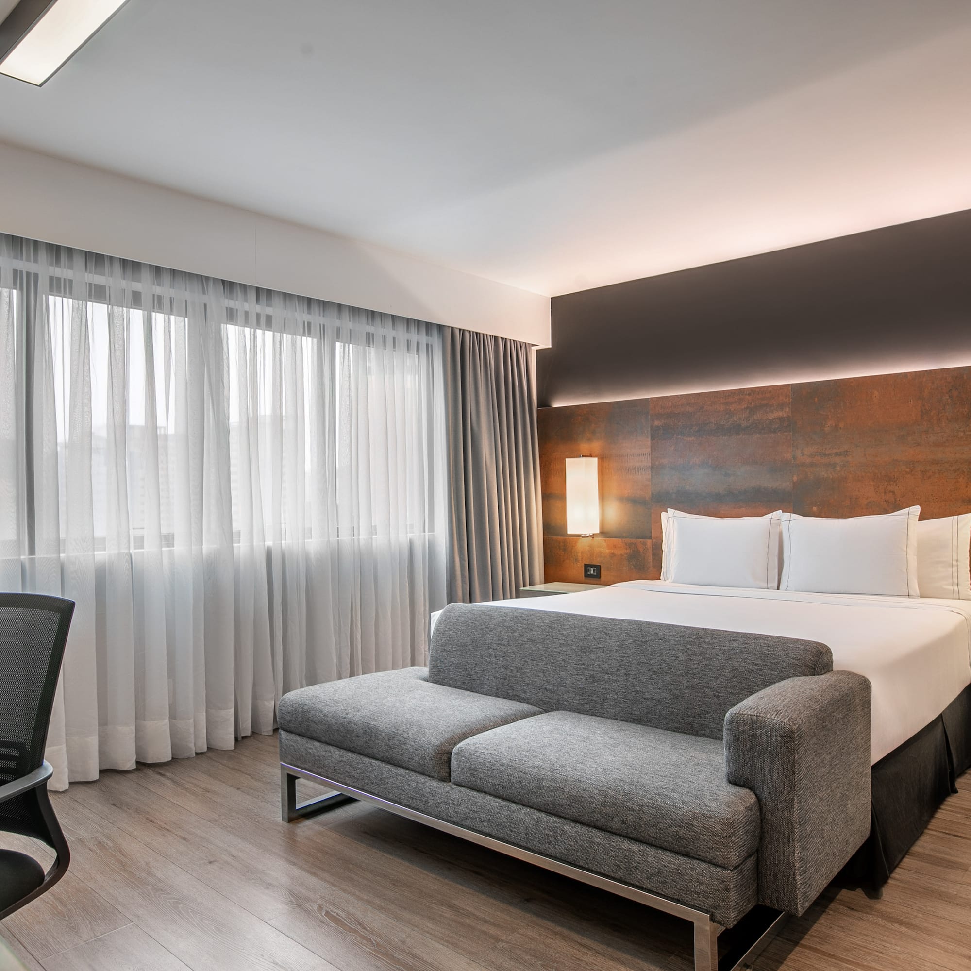 Quarto de hotel moderno com cama de casal, sofá cinza e escrivaninha. - Deluxe Room Queen - Meliá Ibirapuera, São Paulo