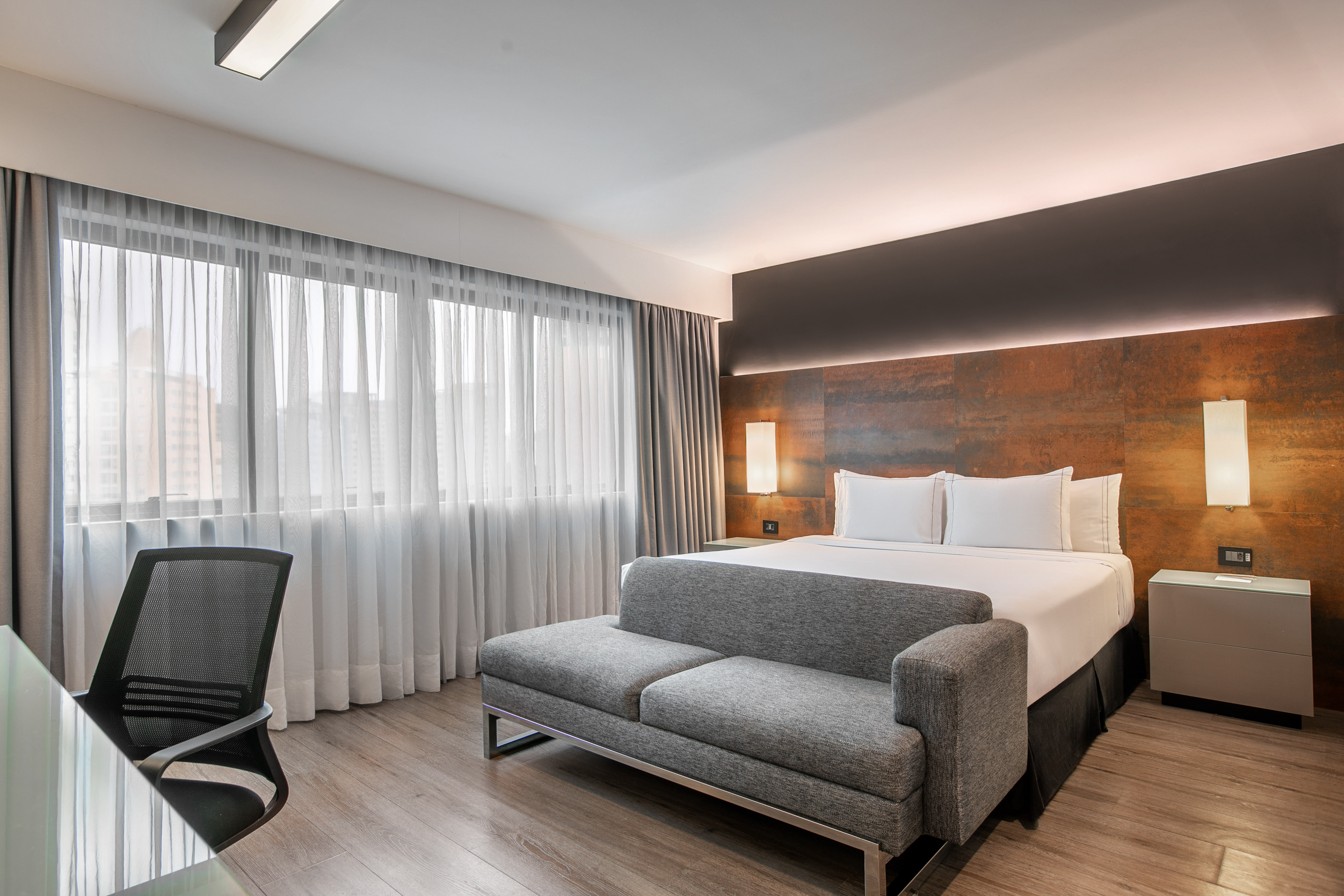 Quarto de hotel moderno com cama de casal, sofá cinza e escrivaninha. - Deluxe Room Queen - Meliá Ibirapuera, São Paulo