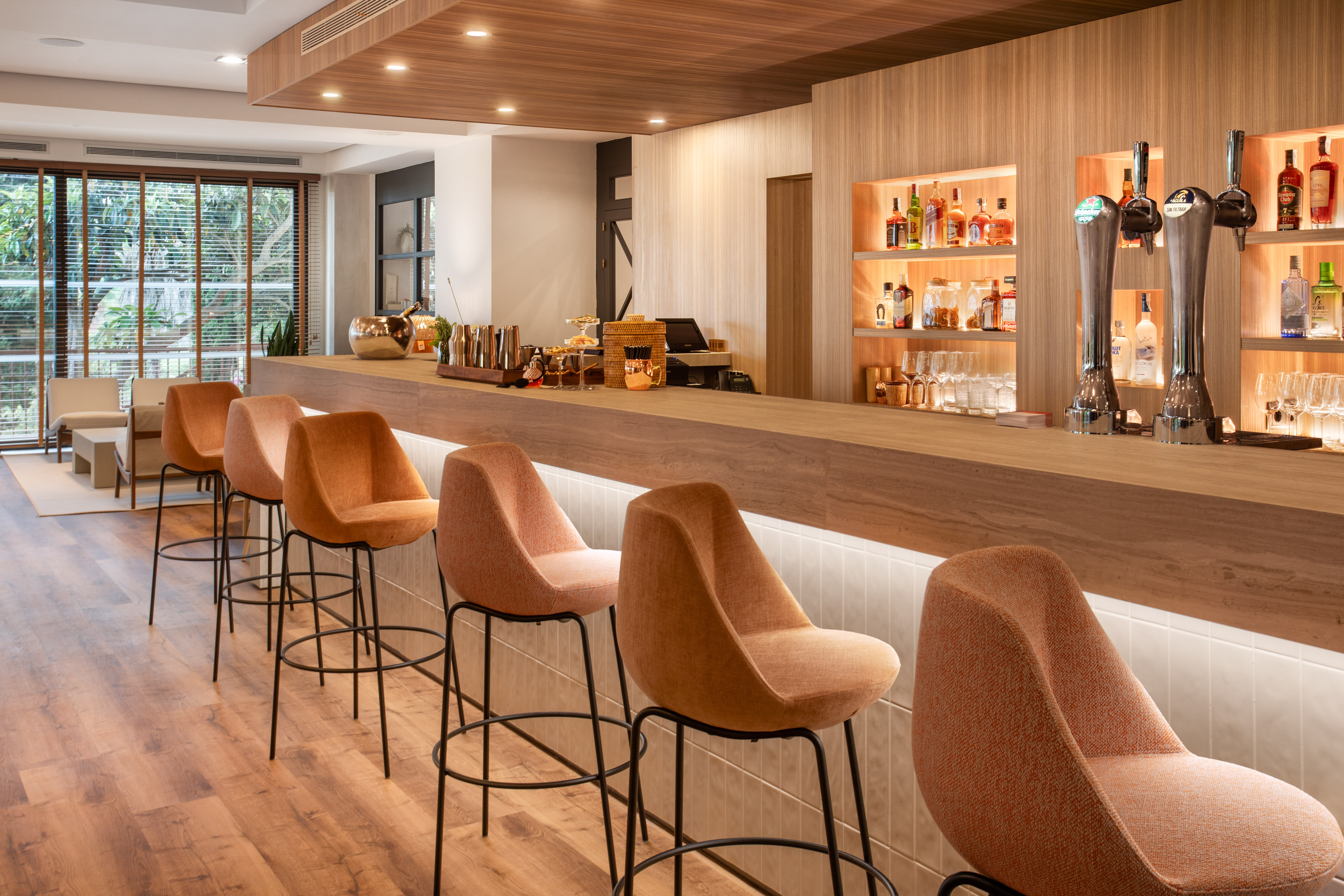 Modern bar with wooden counter, orange bar stools, beer taps, and liquor shelves.