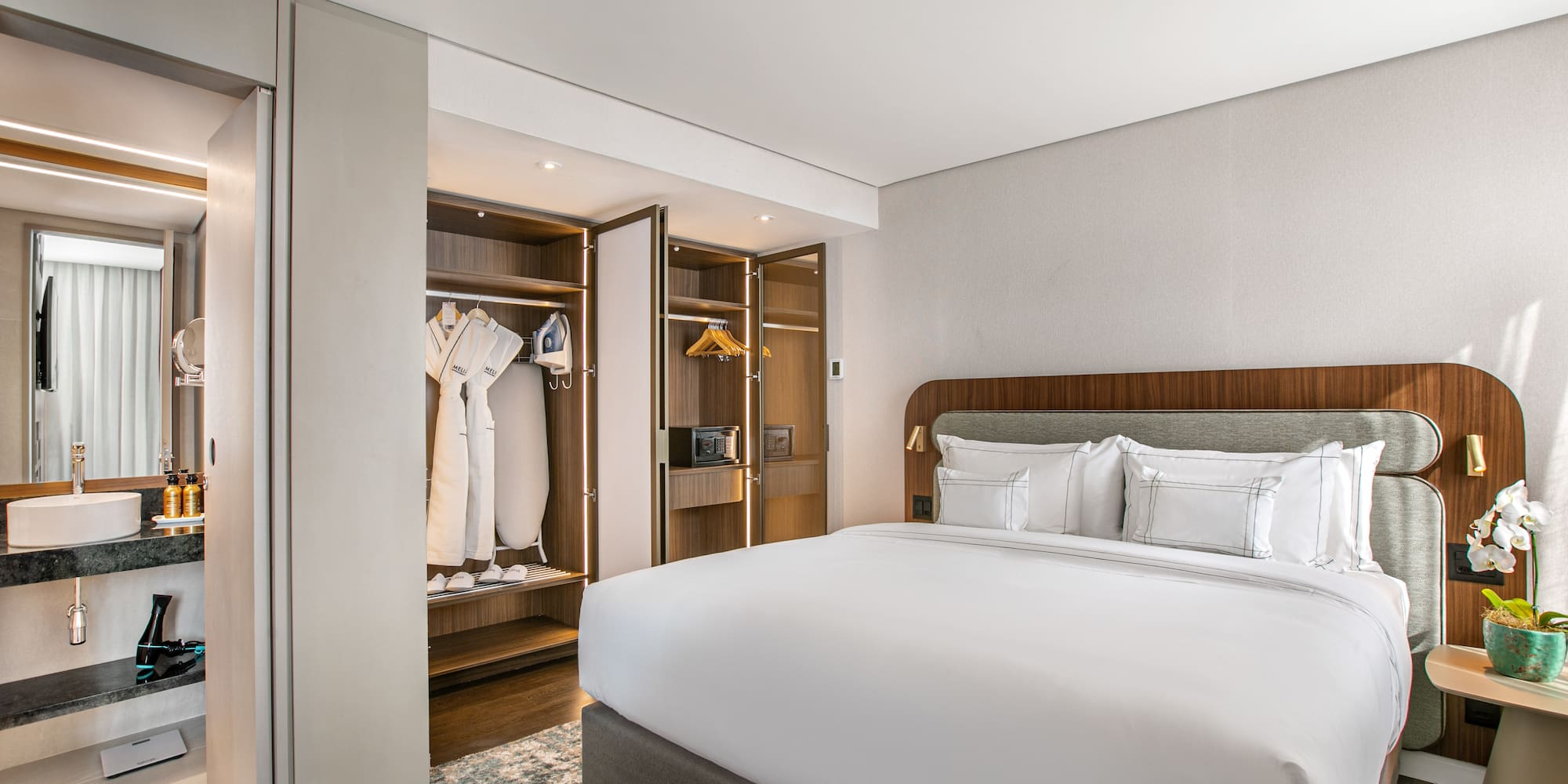 Modern hotel room with king bed, open closet, and adjoining bathroom.