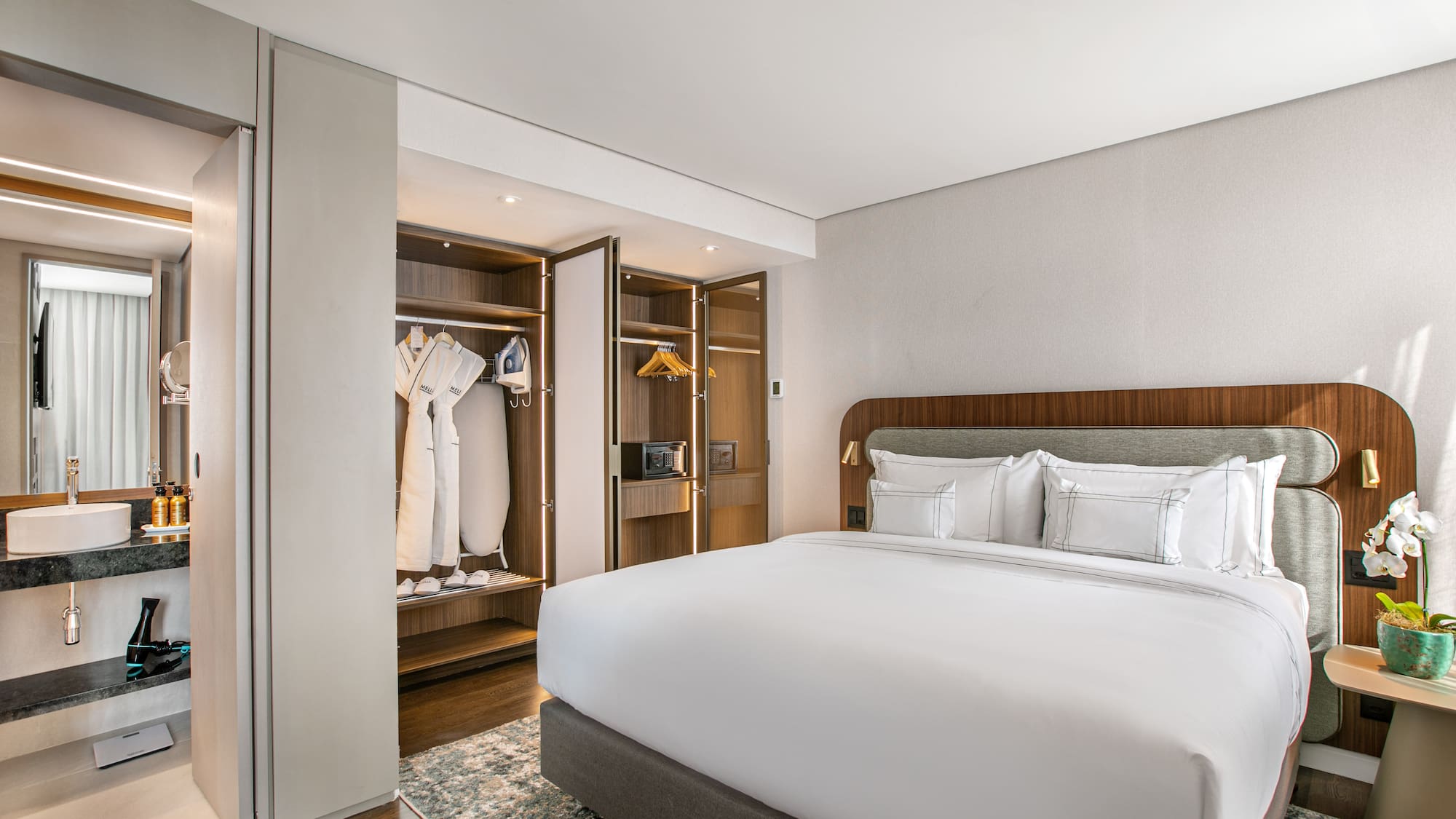 Modern hotel room with king bed, open closet, and adjoining bathroom.