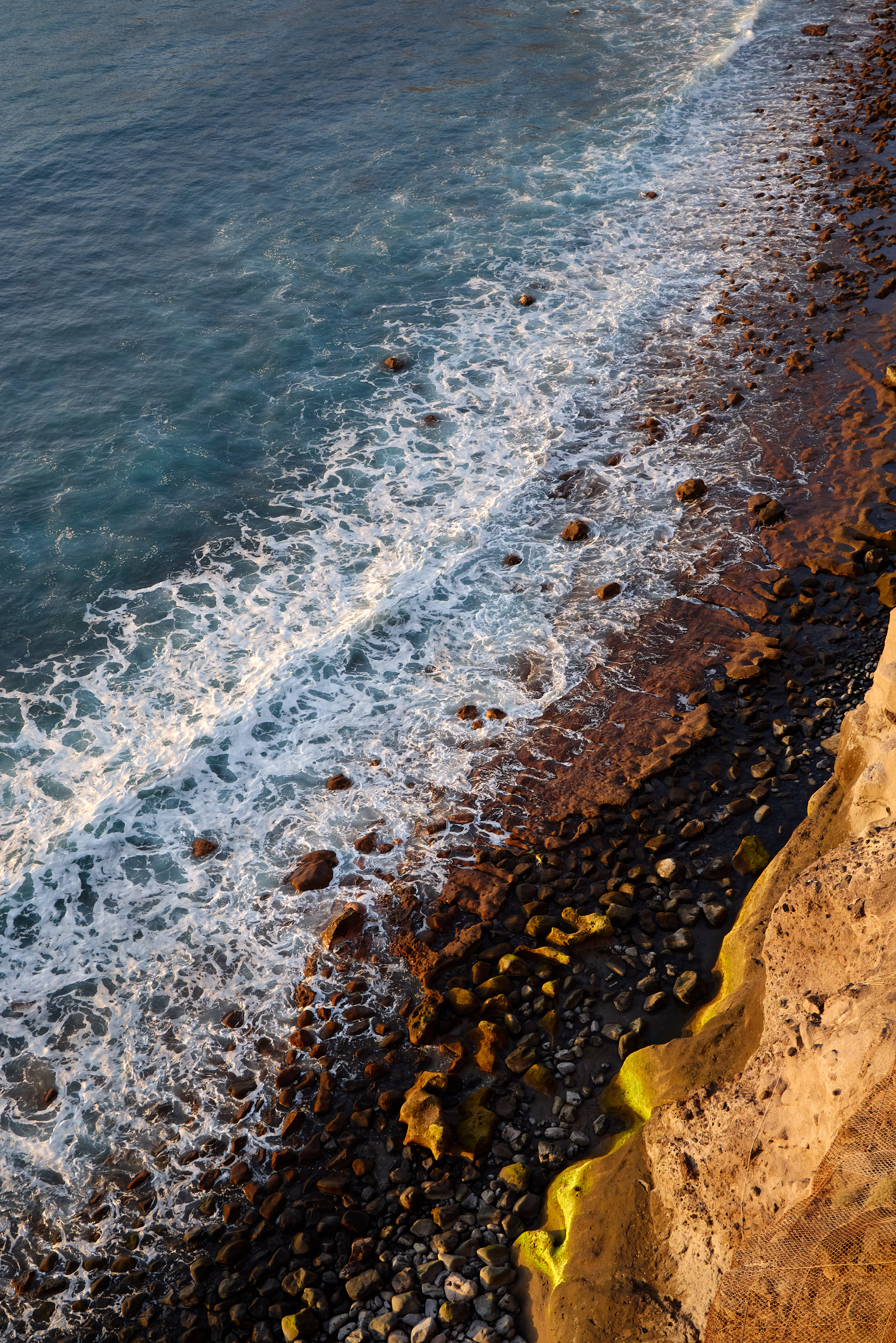 Aerial view of foamy ocean waves crashing on a rocky coastline at golden hour.