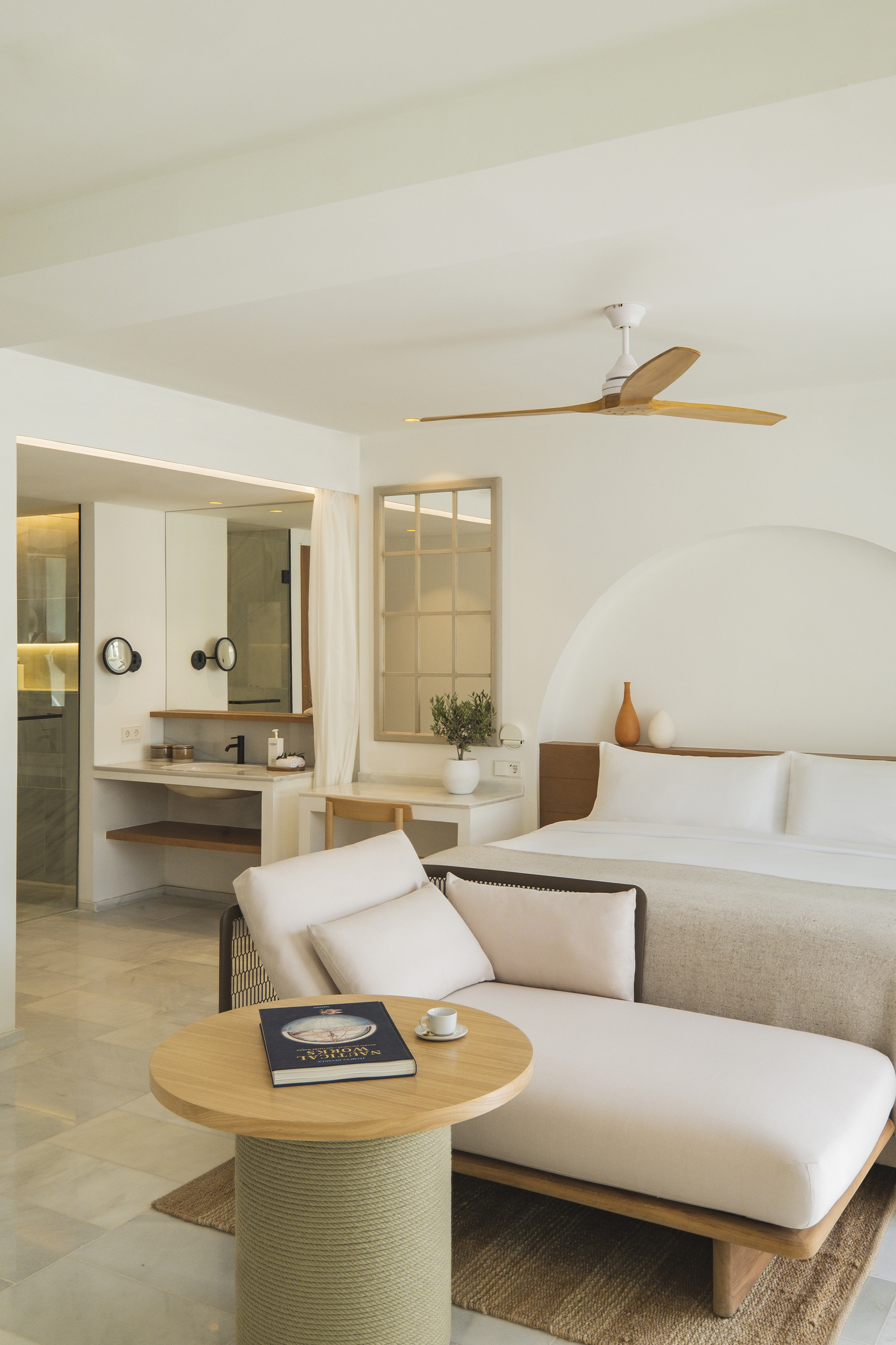 Minimalist hotel room with king bed, chaise lounge, and modern open-concept bathroom.
