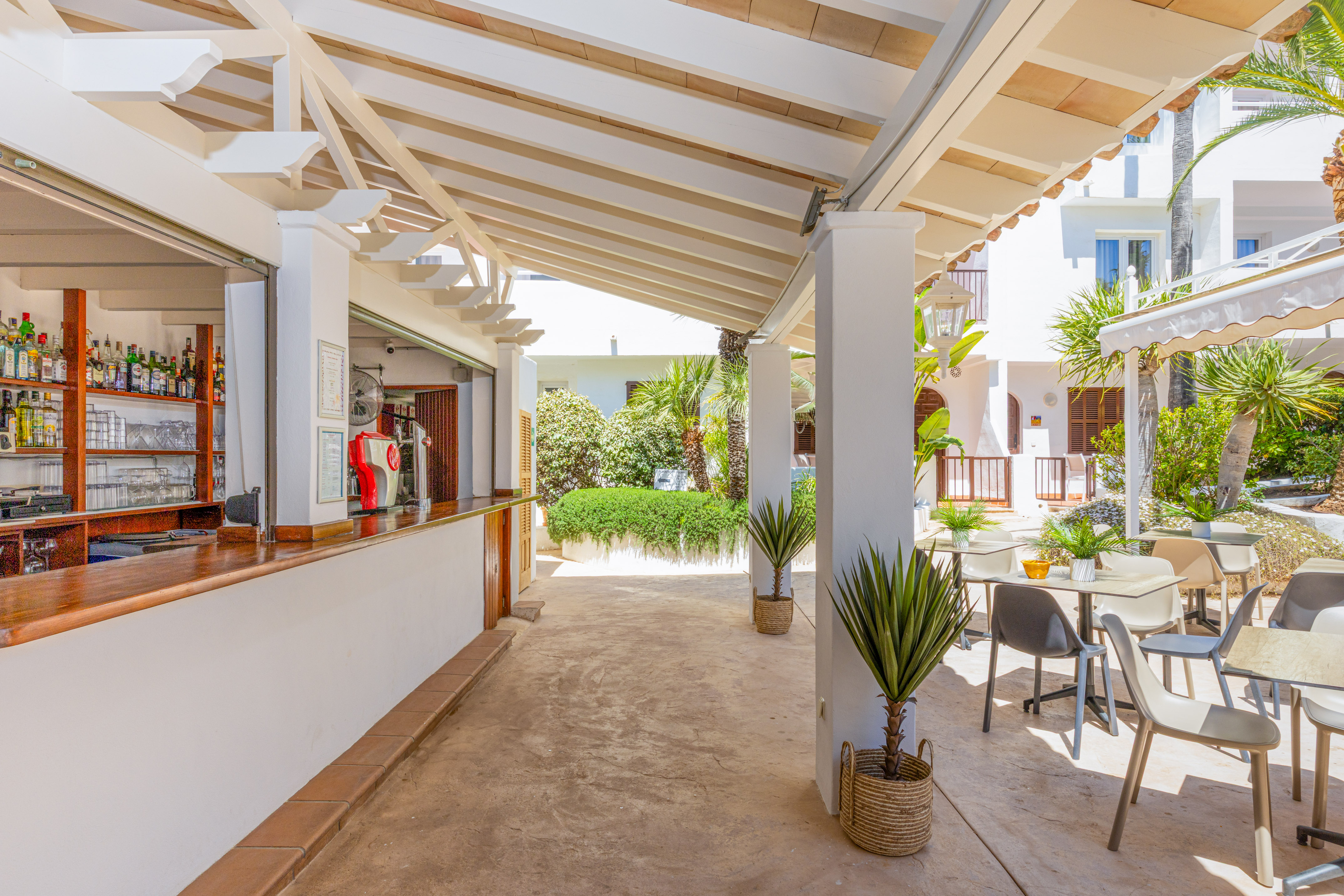 Covered outdoor bar and dining area at a sunny hotel resort with lush plants.