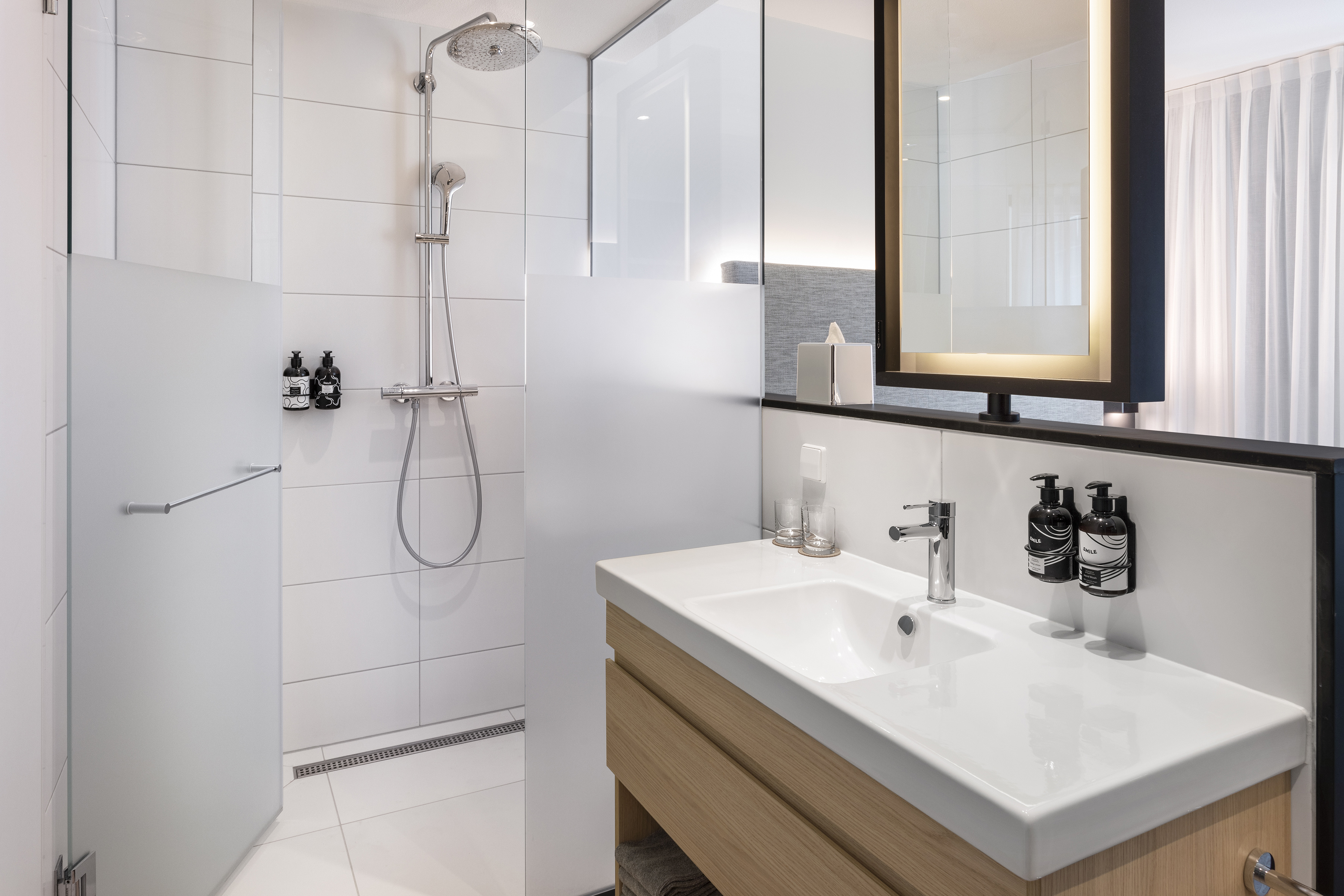Modern bathroom with walk-in shower, white tiles, wood vanity, and modern mirror.