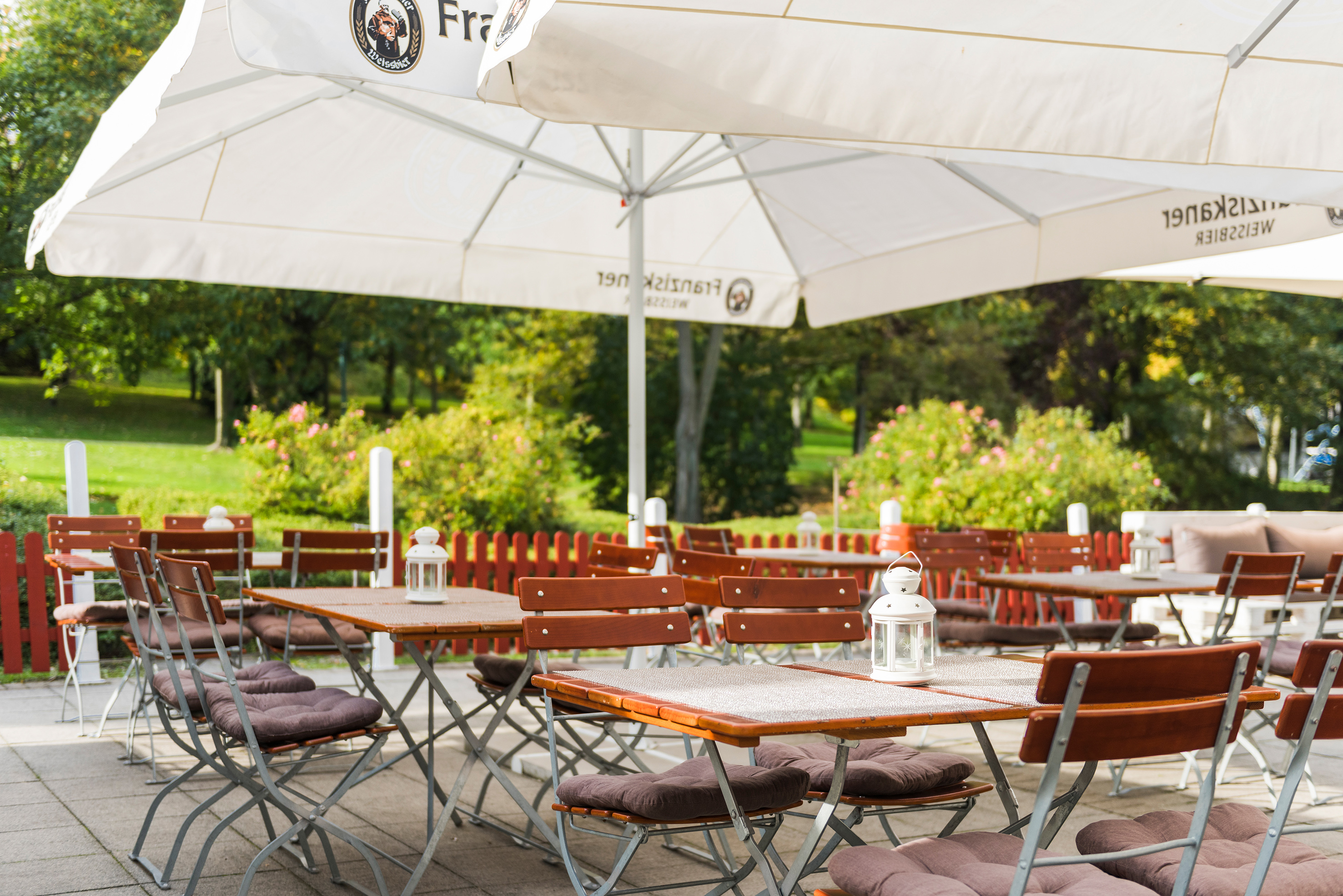Outdoor cafe patio with wooden tables, cushioned chairs, and white umbrellas.
