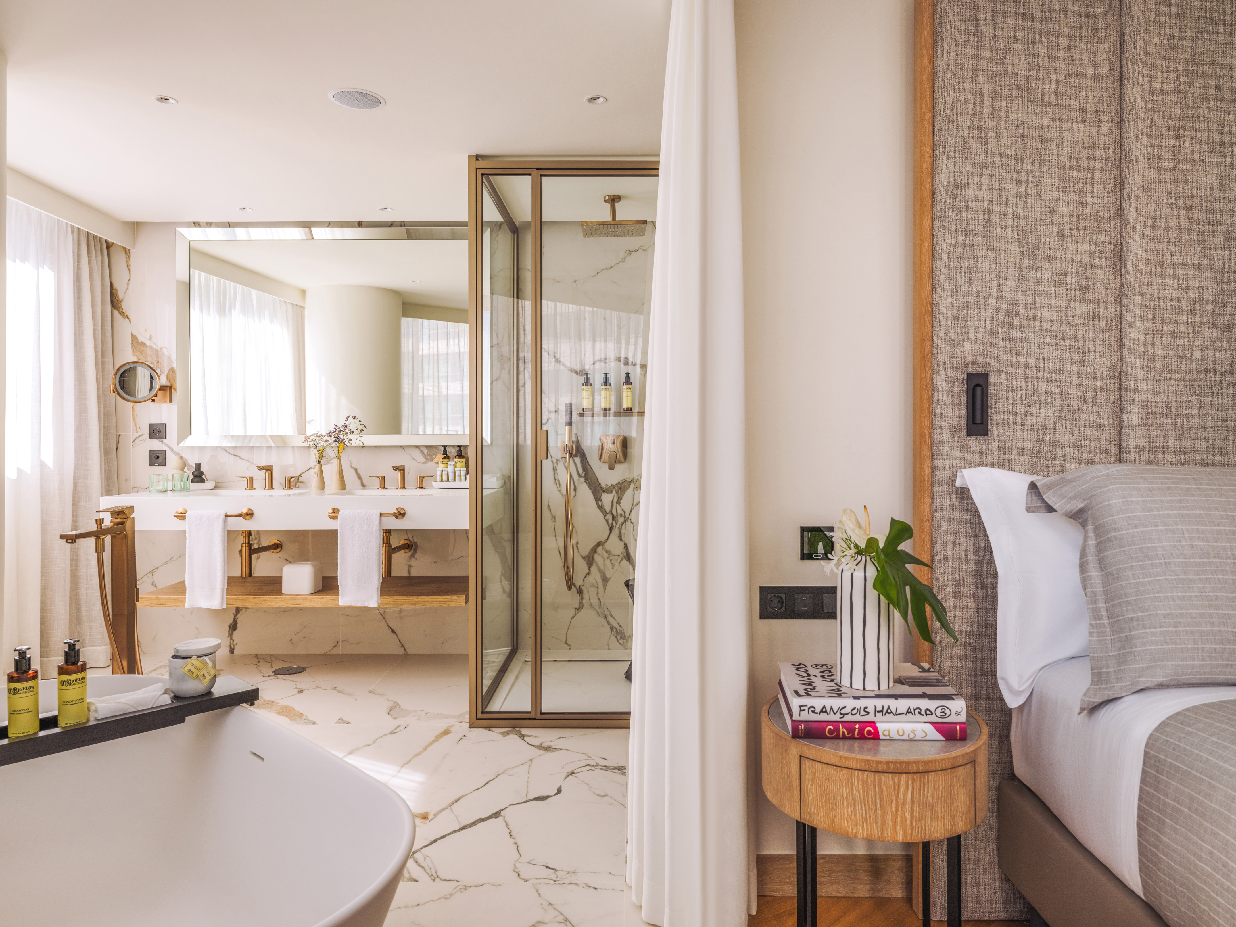 Elegant hotel suite: marble bathroom, freestanding tub, glass shower, bed.