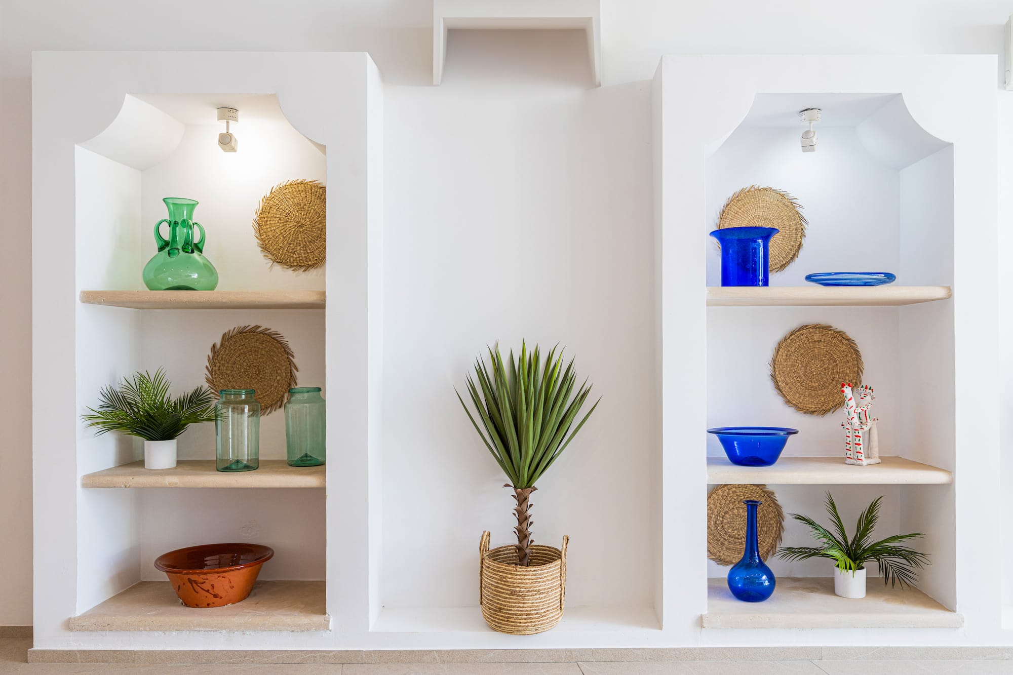 White wall niches with plants, blue and green glass decor, straw accents.
