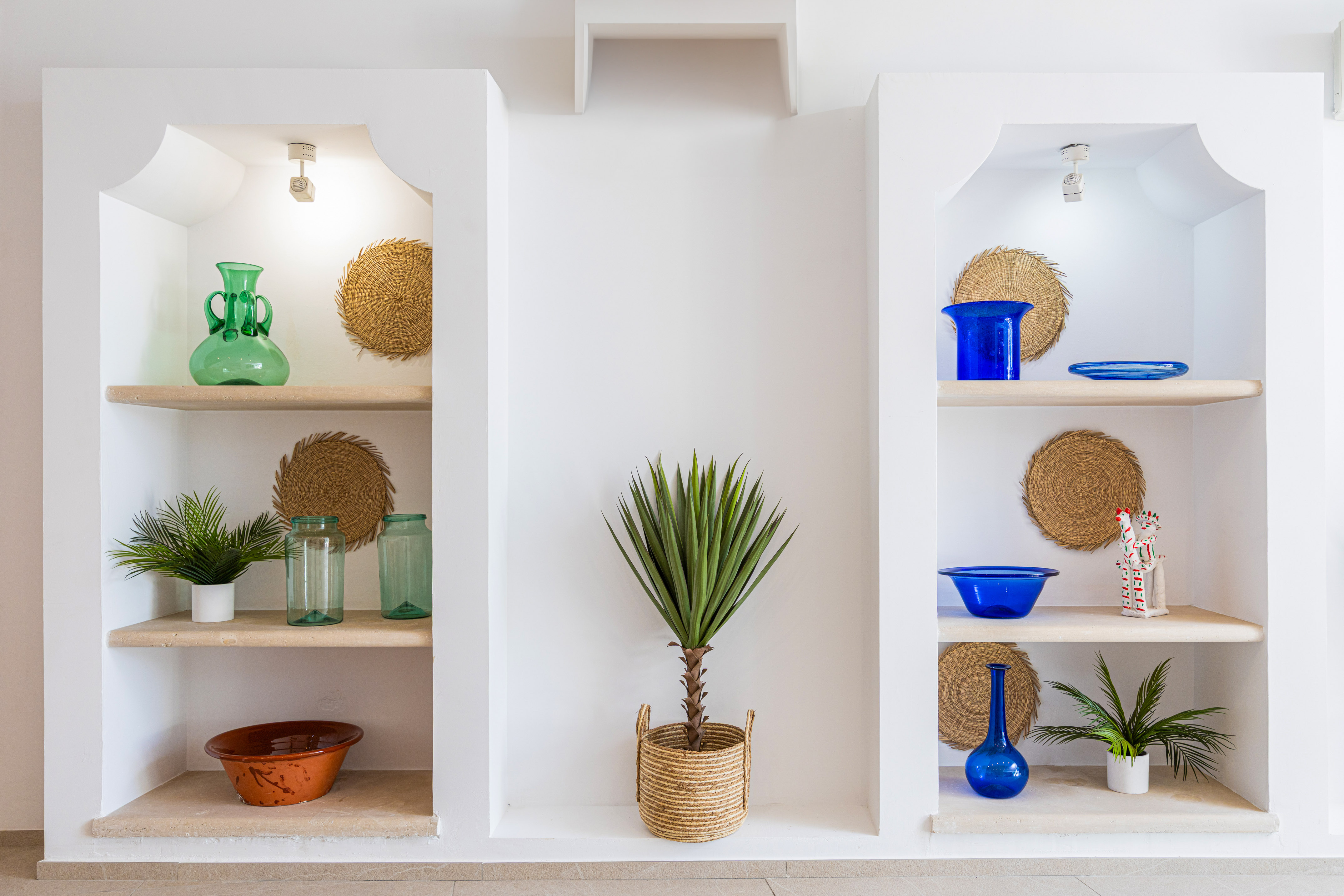 White wall niches with plants, blue and green glass decor, straw accents.