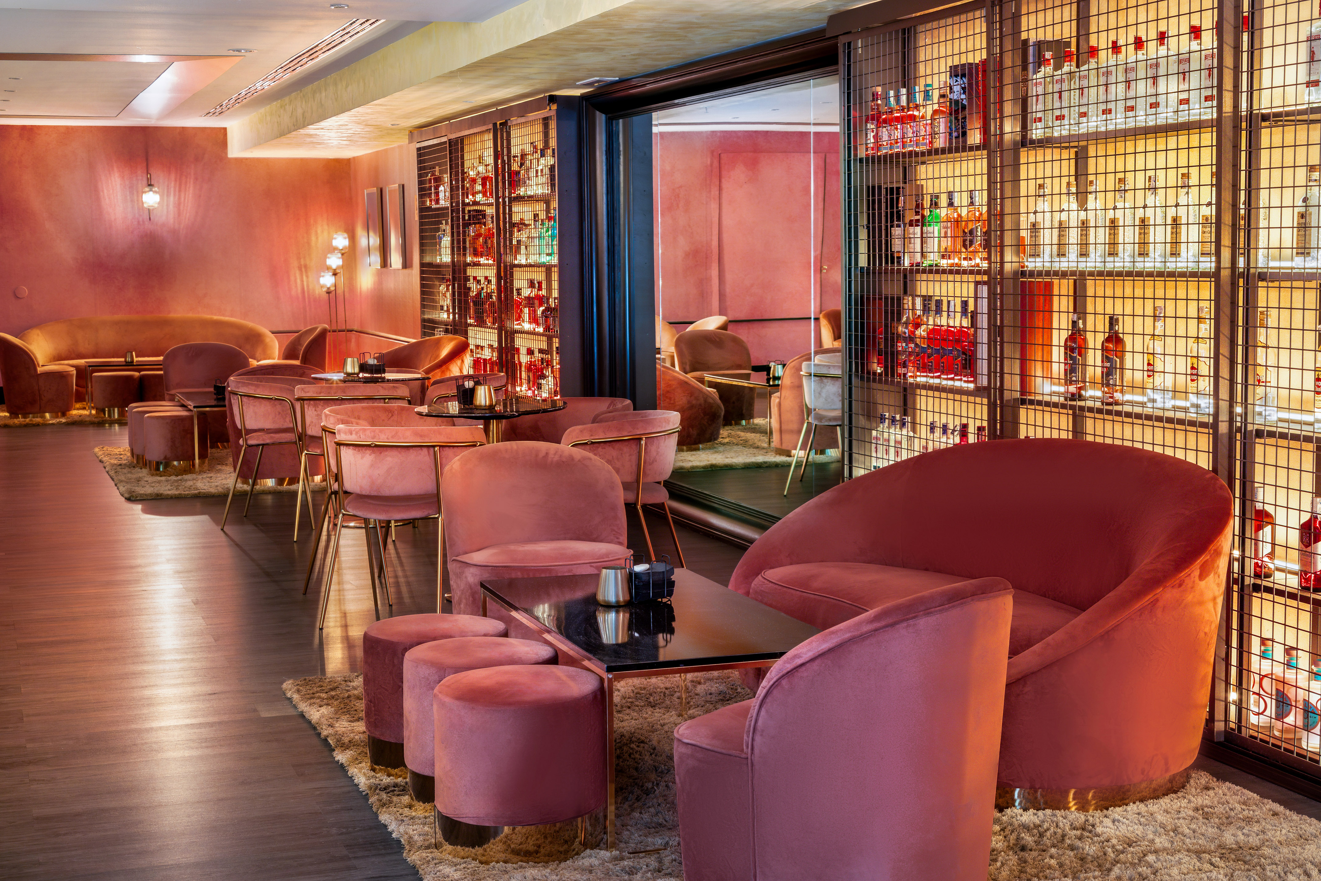 Pink velvet seating in a modern, luxurious bar with illuminated bottle shelves.