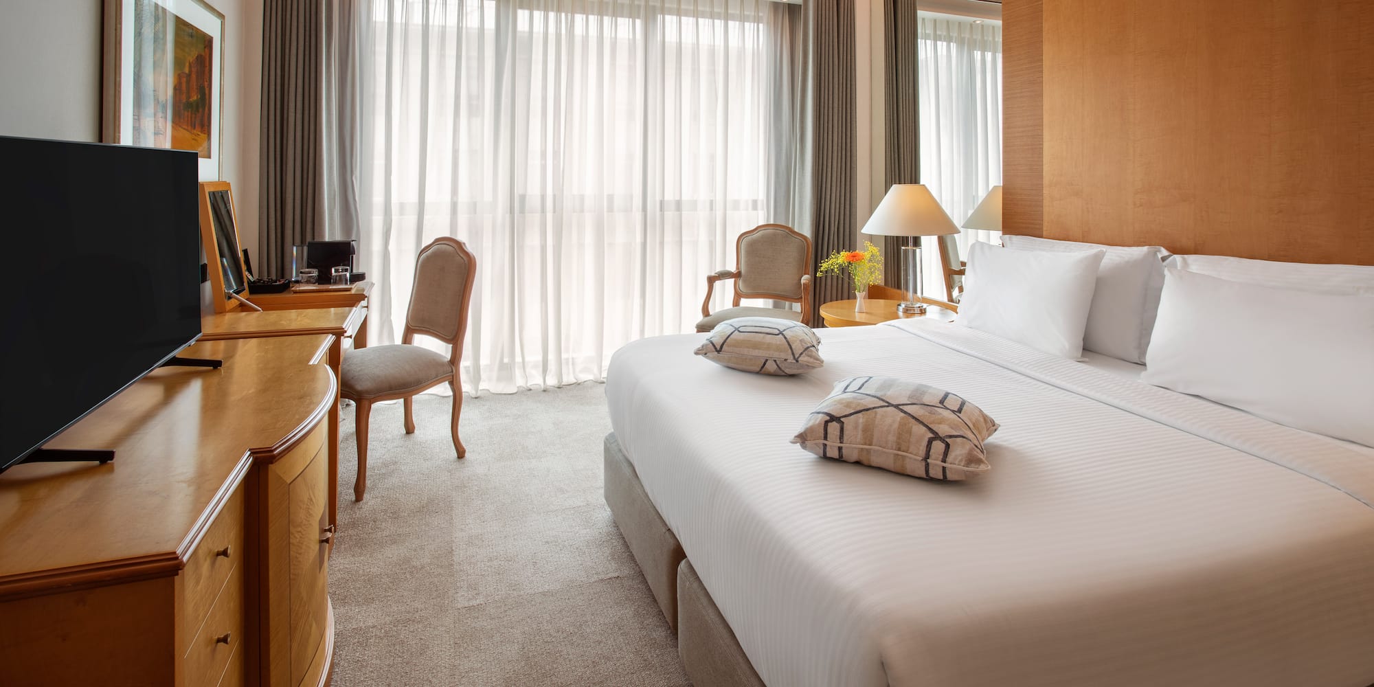 Luxury hotel room with king bed, flat-screen TV, wooden desk, and bright window.