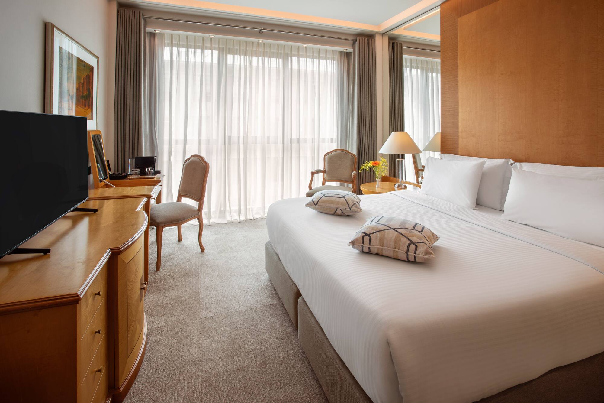 Luxury hotel room with king bed, flat-screen TV, wooden desk, and bright window.