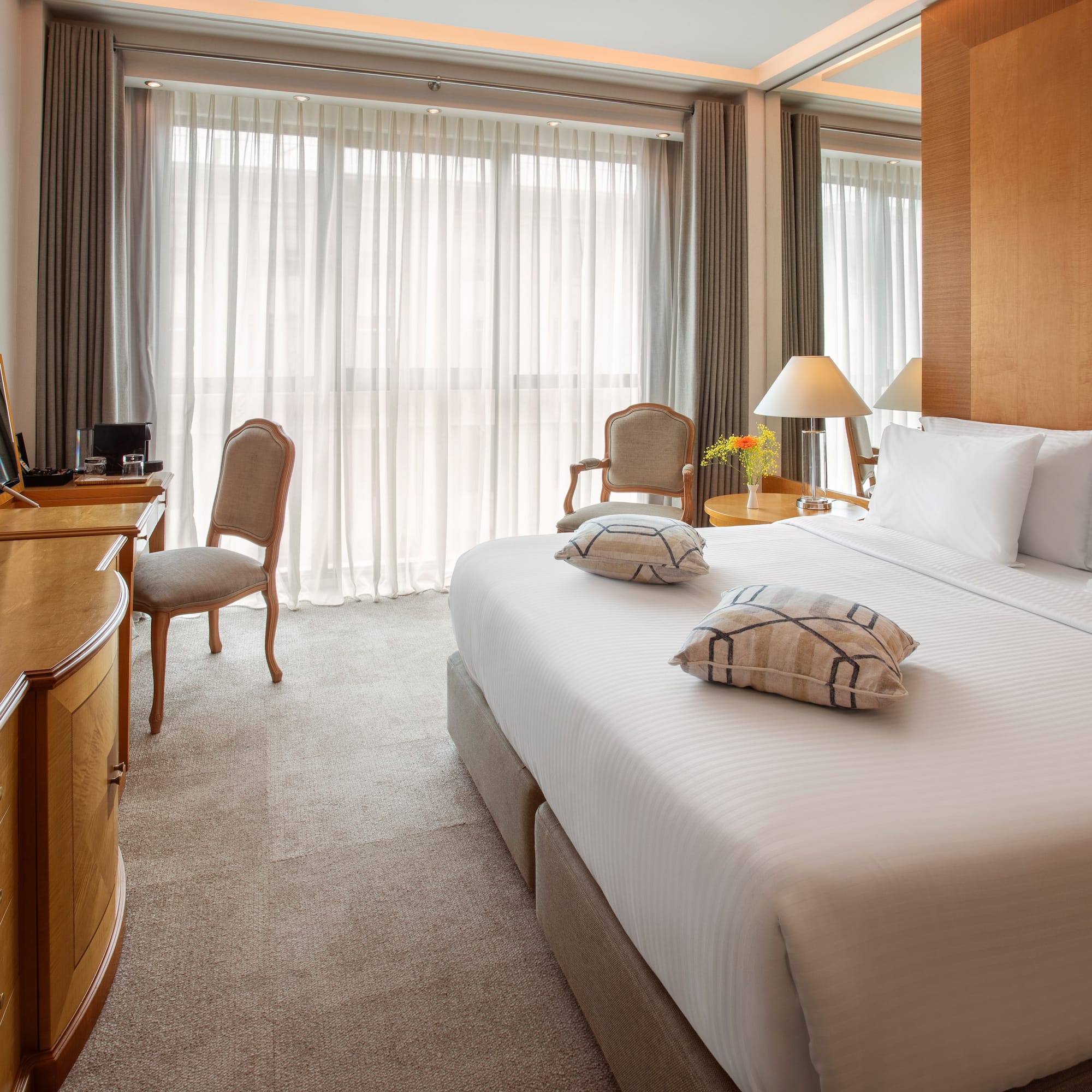 Luxury hotel room with king bed, flat-screen TV, wooden desk, and bright window.