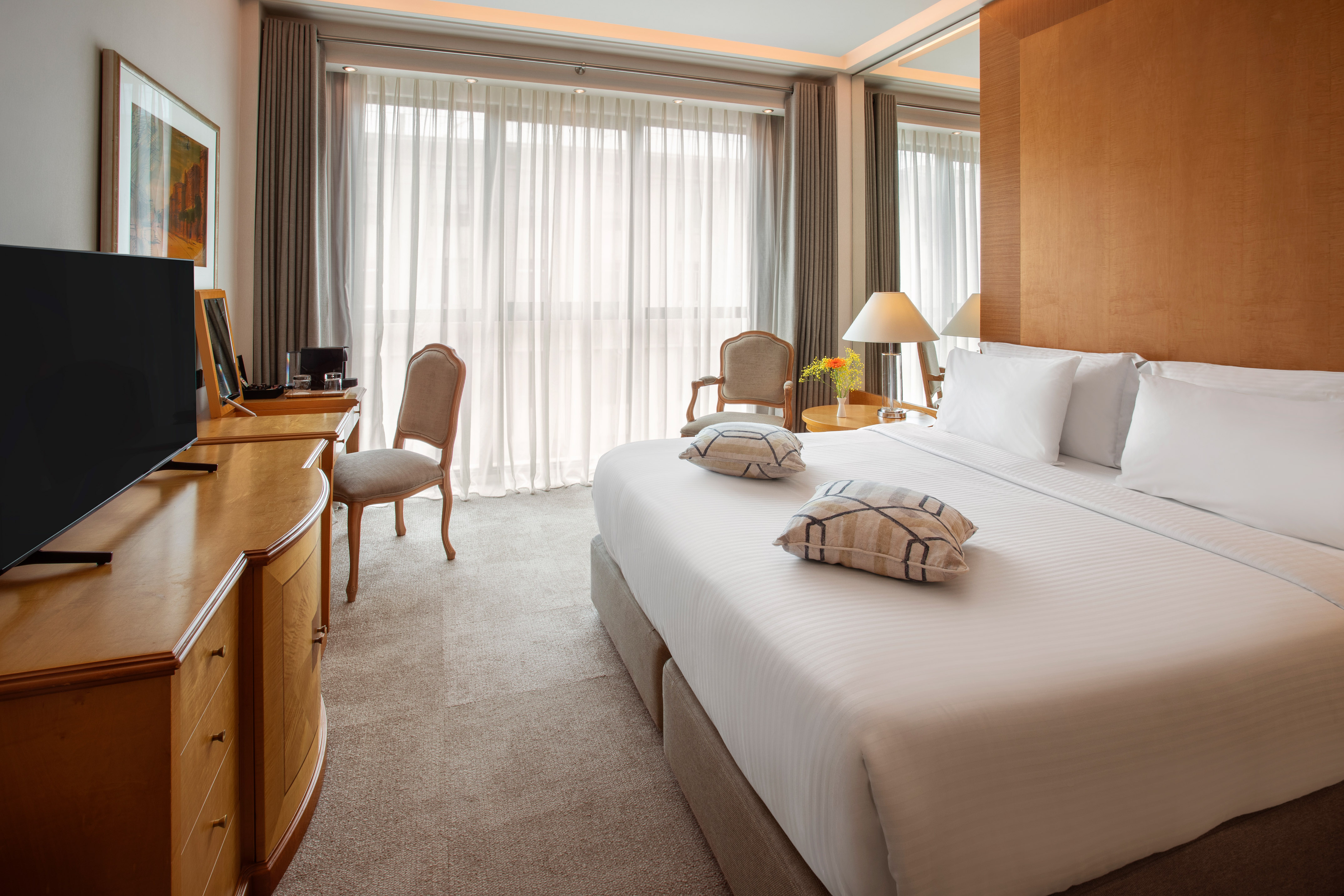 Luxury hotel room with king bed, flat-screen TV, wooden desk, and bright window.