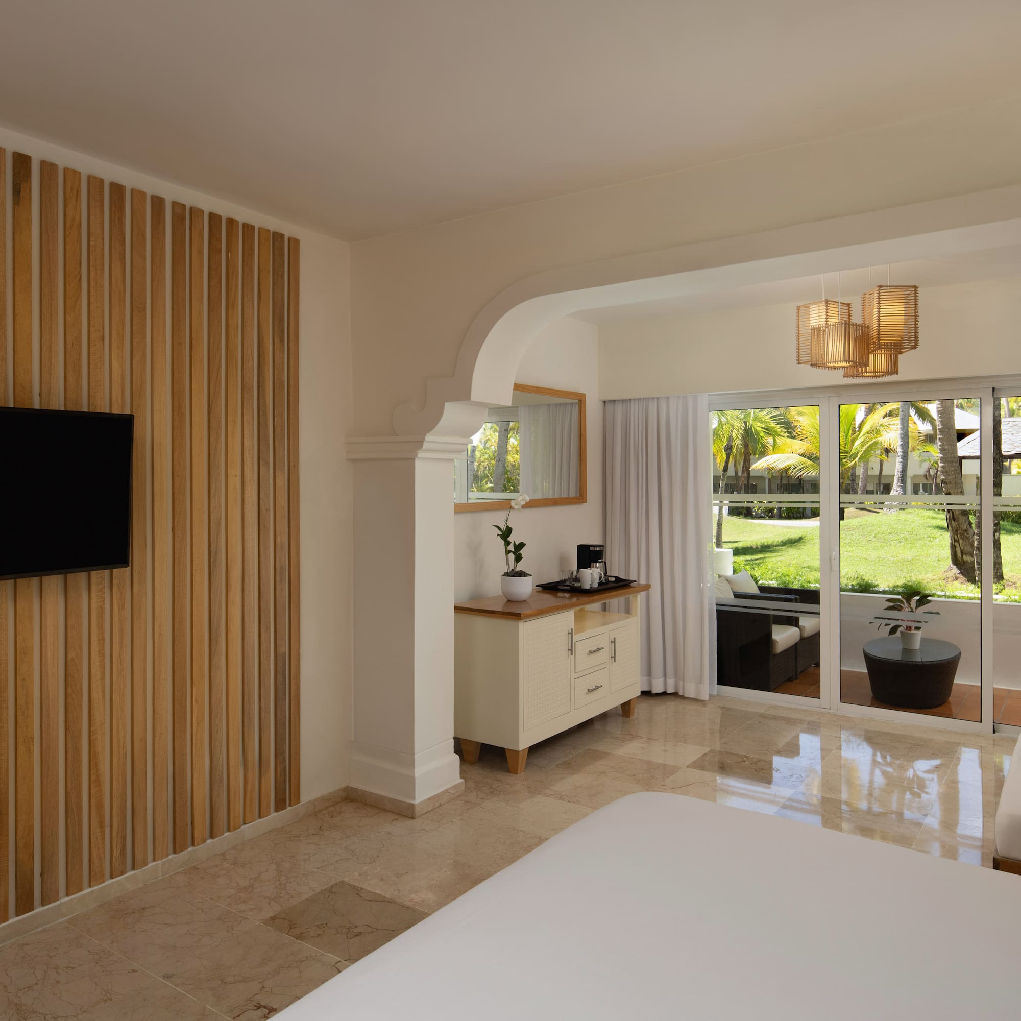 Modern resort bedroom with TV, wood accent wall, and tropical patio view.