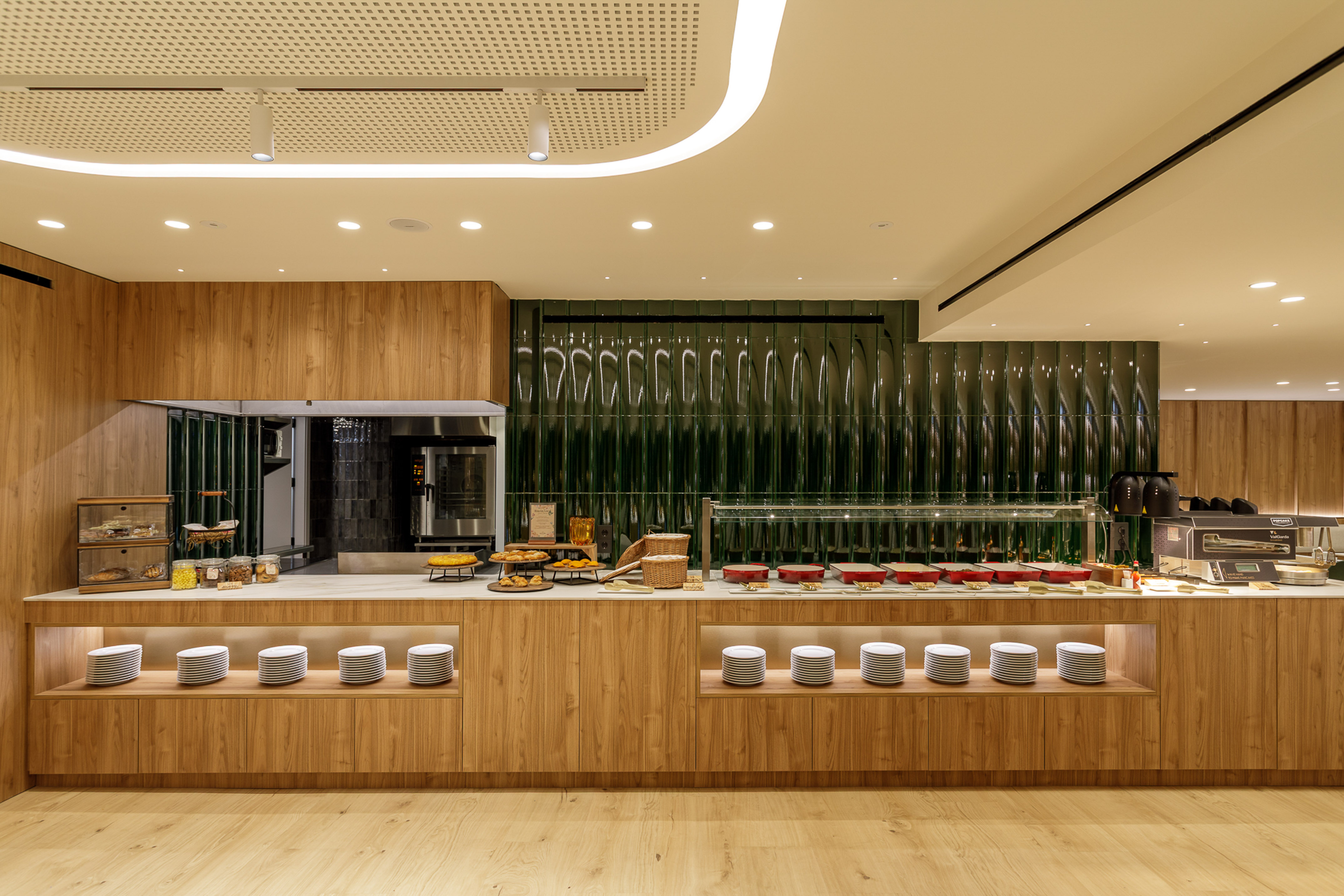 Modern hotel breakfast buffet with wooden counters, green textured wall, and prepared food.