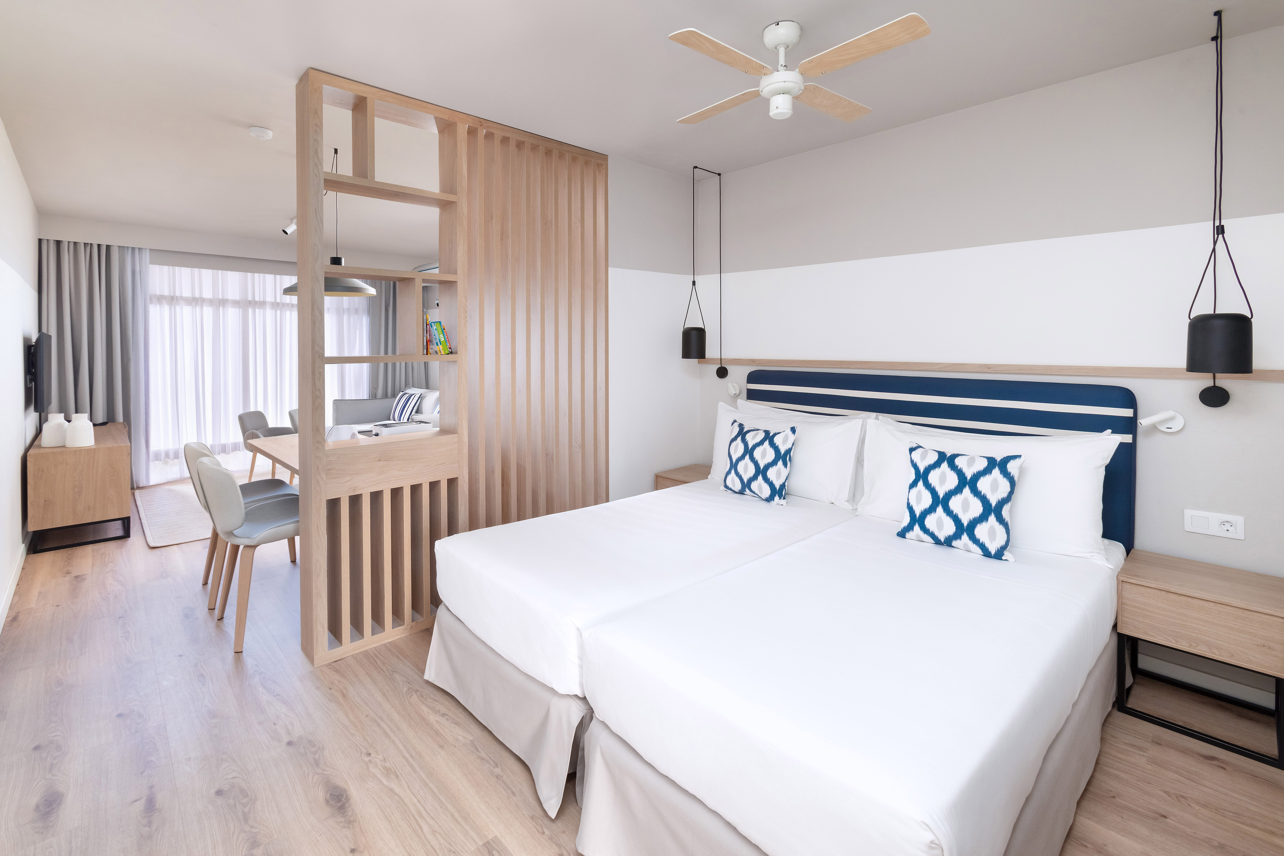 Modern hotel bedroom with twin beds, blue accents, and wooden room divider.