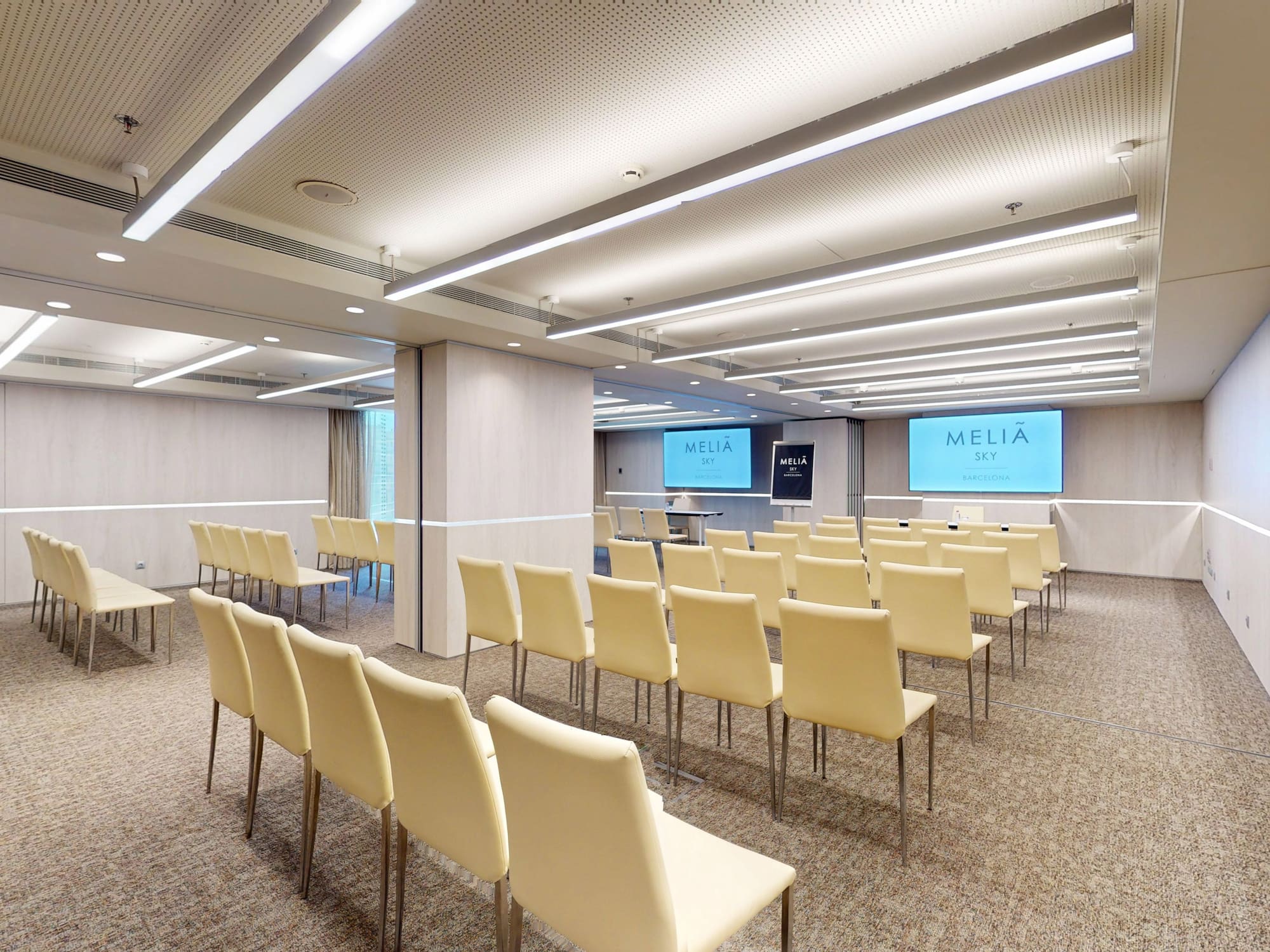 Empty Meliã Sky Barcelona conference room with cream chairs and dual screens.