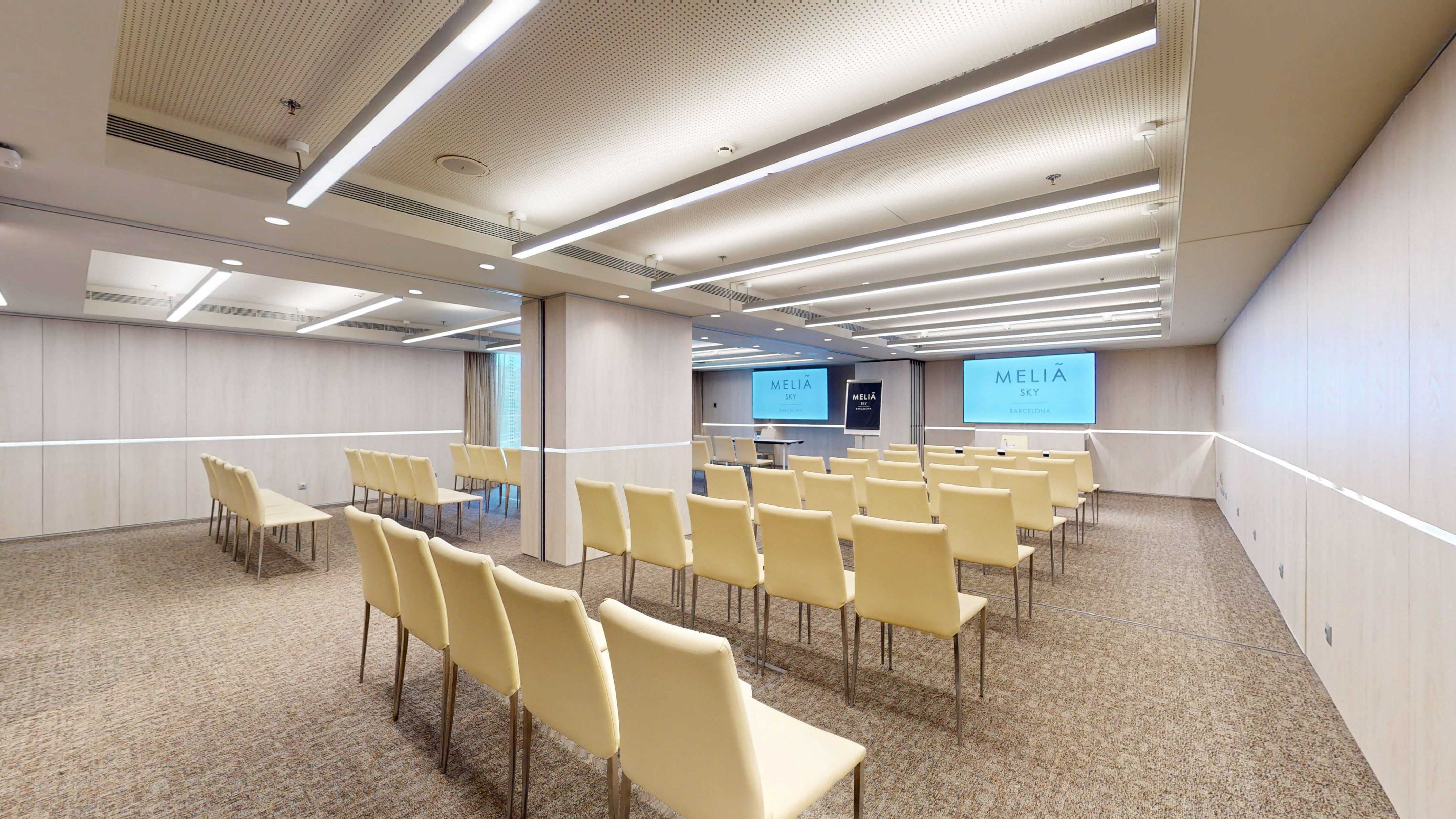 Empty Meliã Sky Barcelona conference room with cream chairs and dual screens.