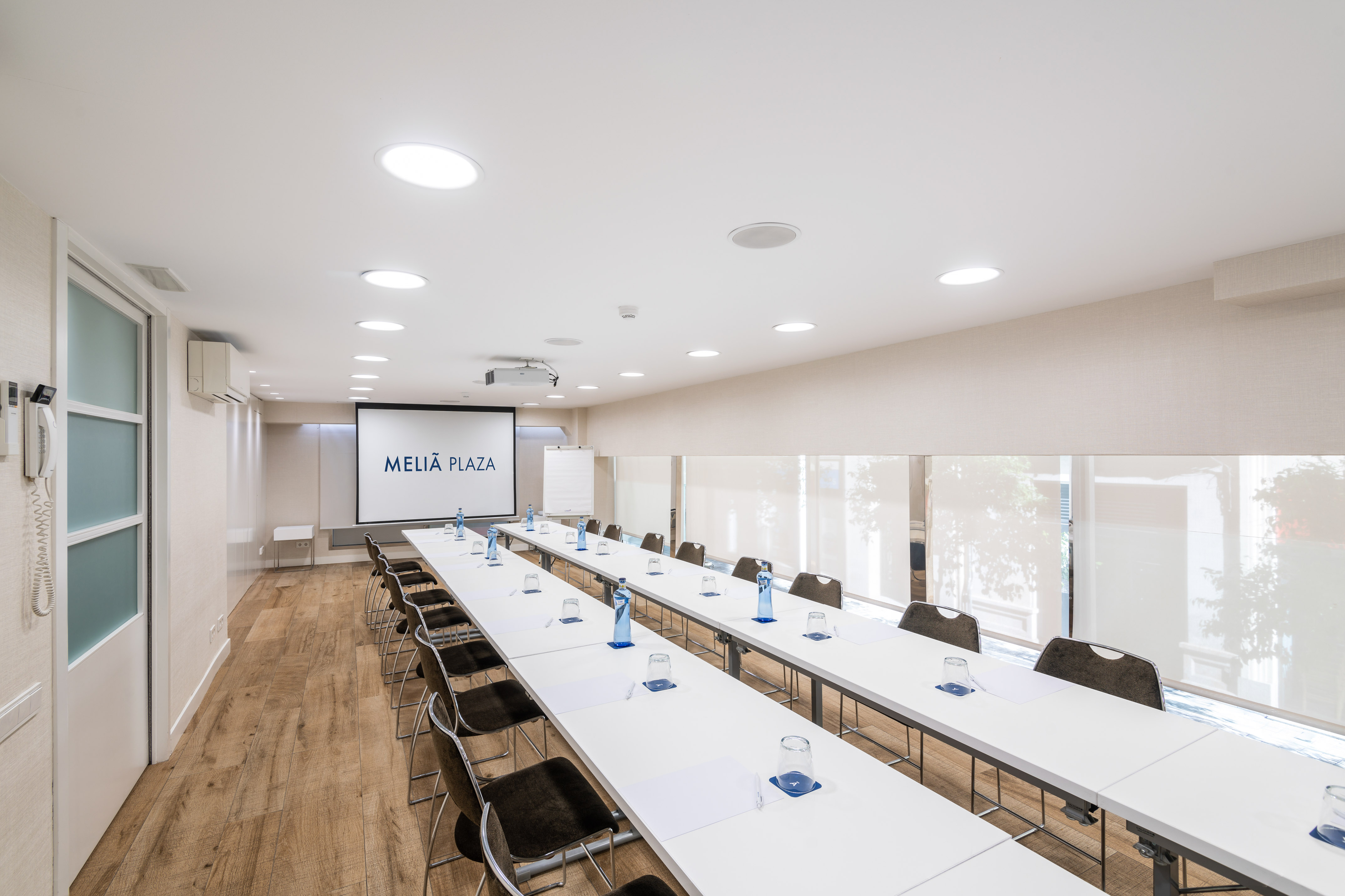 Modern Meliá Plaza conference room with tables, chairs, and projector screen.