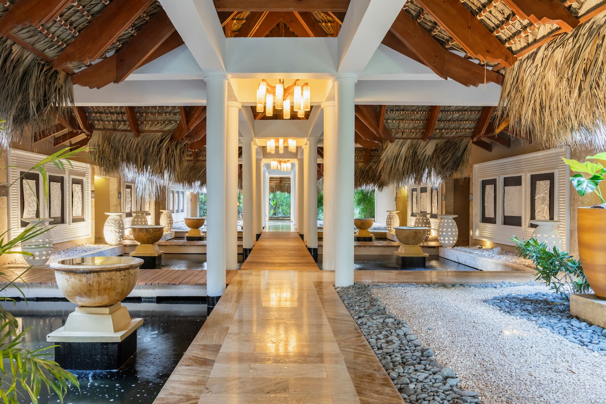 Tropical resort lobby with thatched roof, water features, and modern lights.