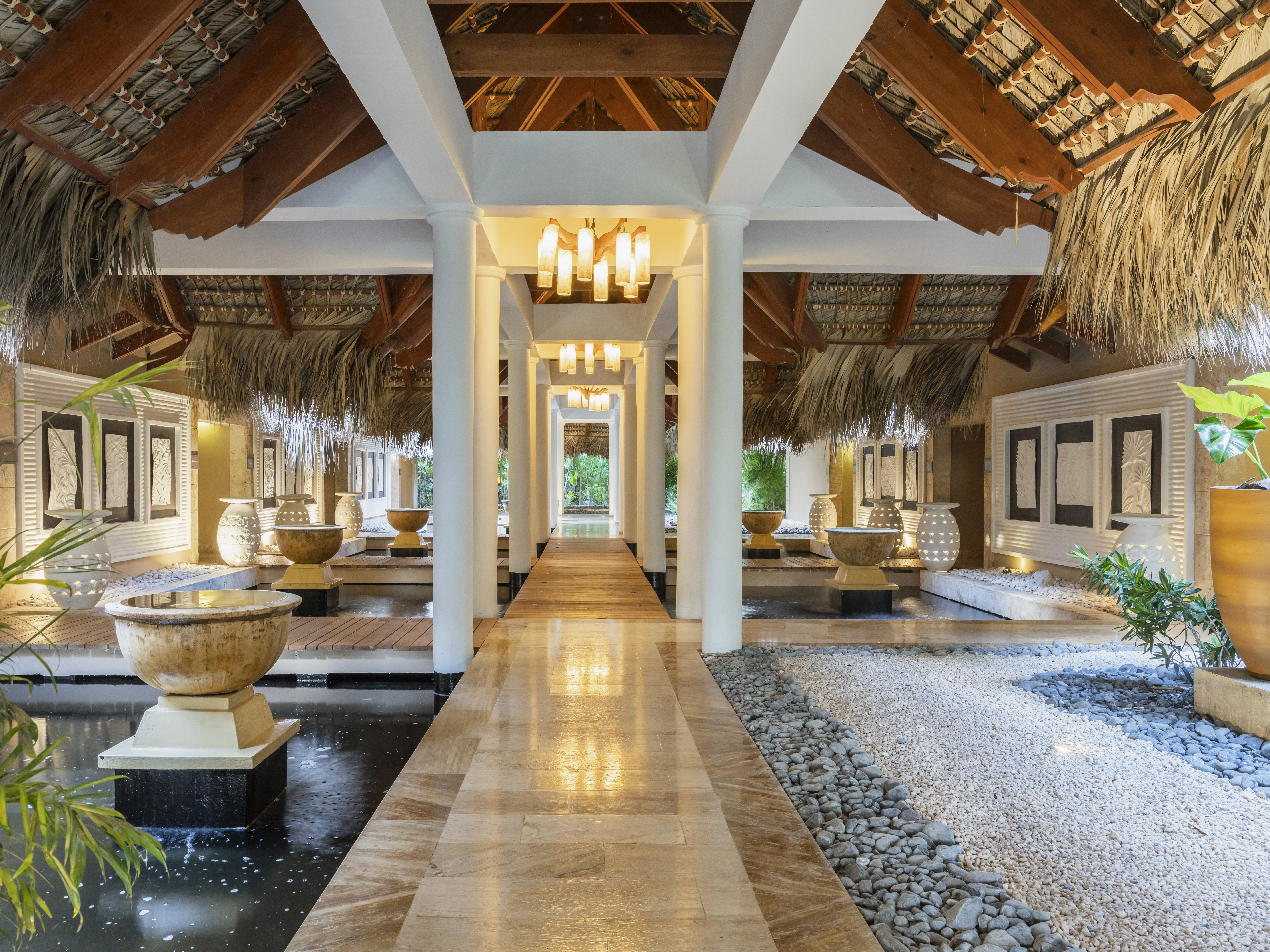 Tropical resort lobby with thatched roof, water features, and modern lights.