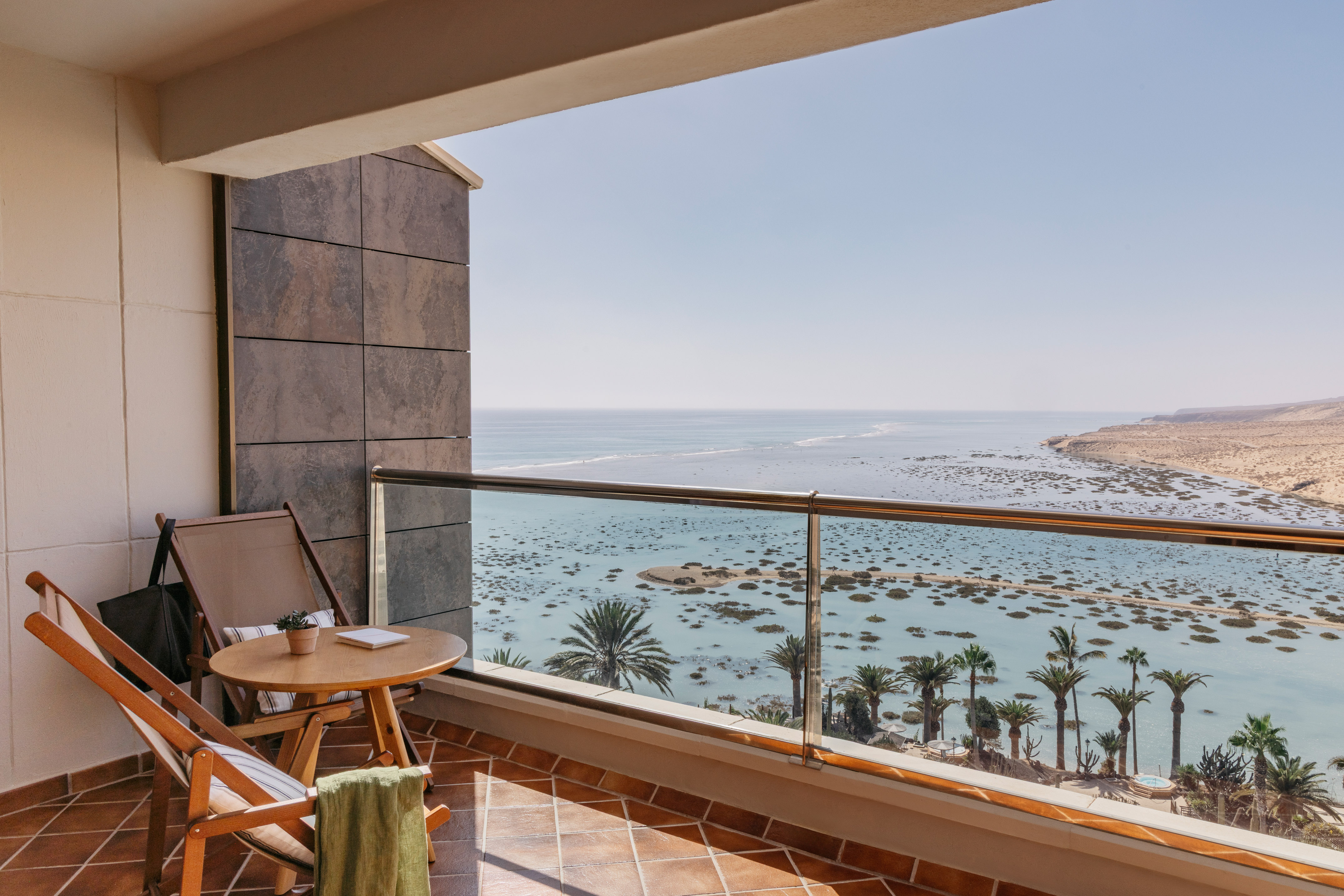 Balcony with ocean, lagoon, palm trees, and desert coast view.