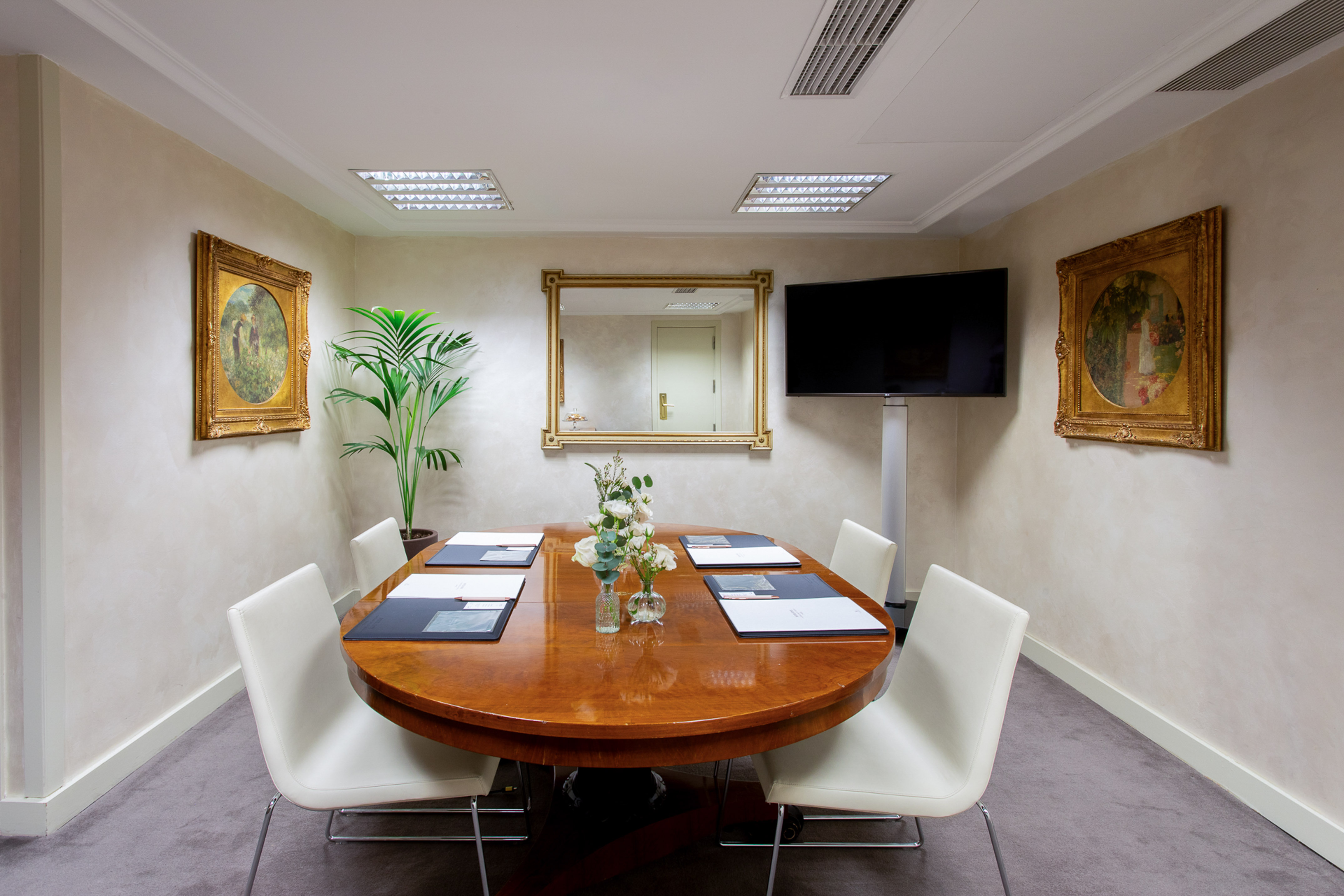 Professional meeting room with oval wooden table, white chairs, TV, and artwork.