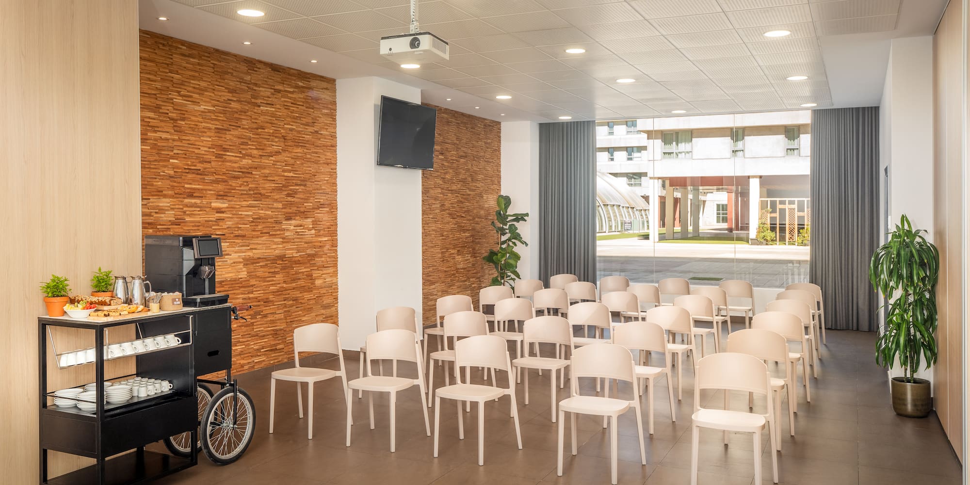 Modern meeting room with rows of chairs, projector, TV, and coffee station.