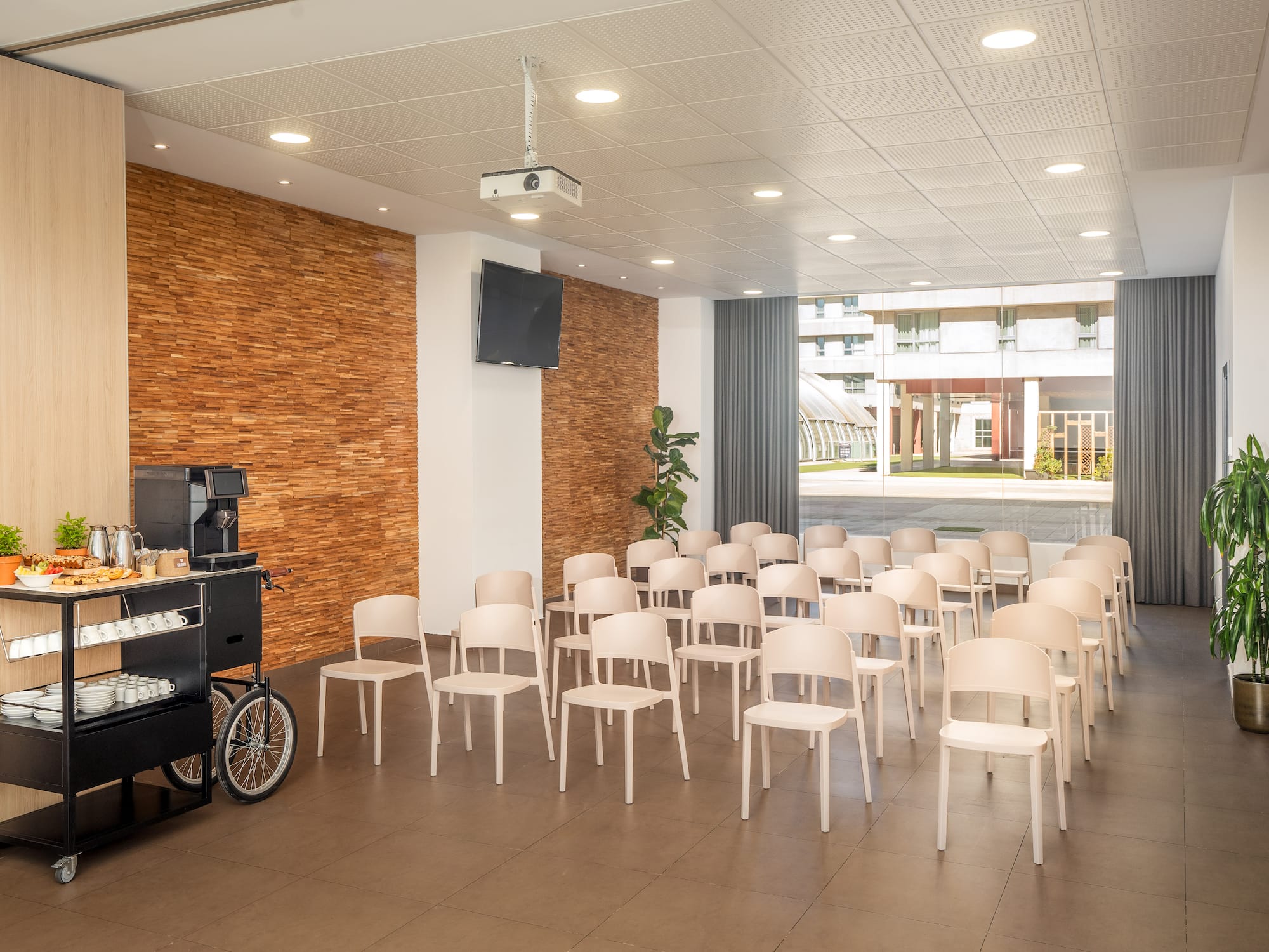 Modern conference room with beige chairs, projector, TV, and coffee break station.