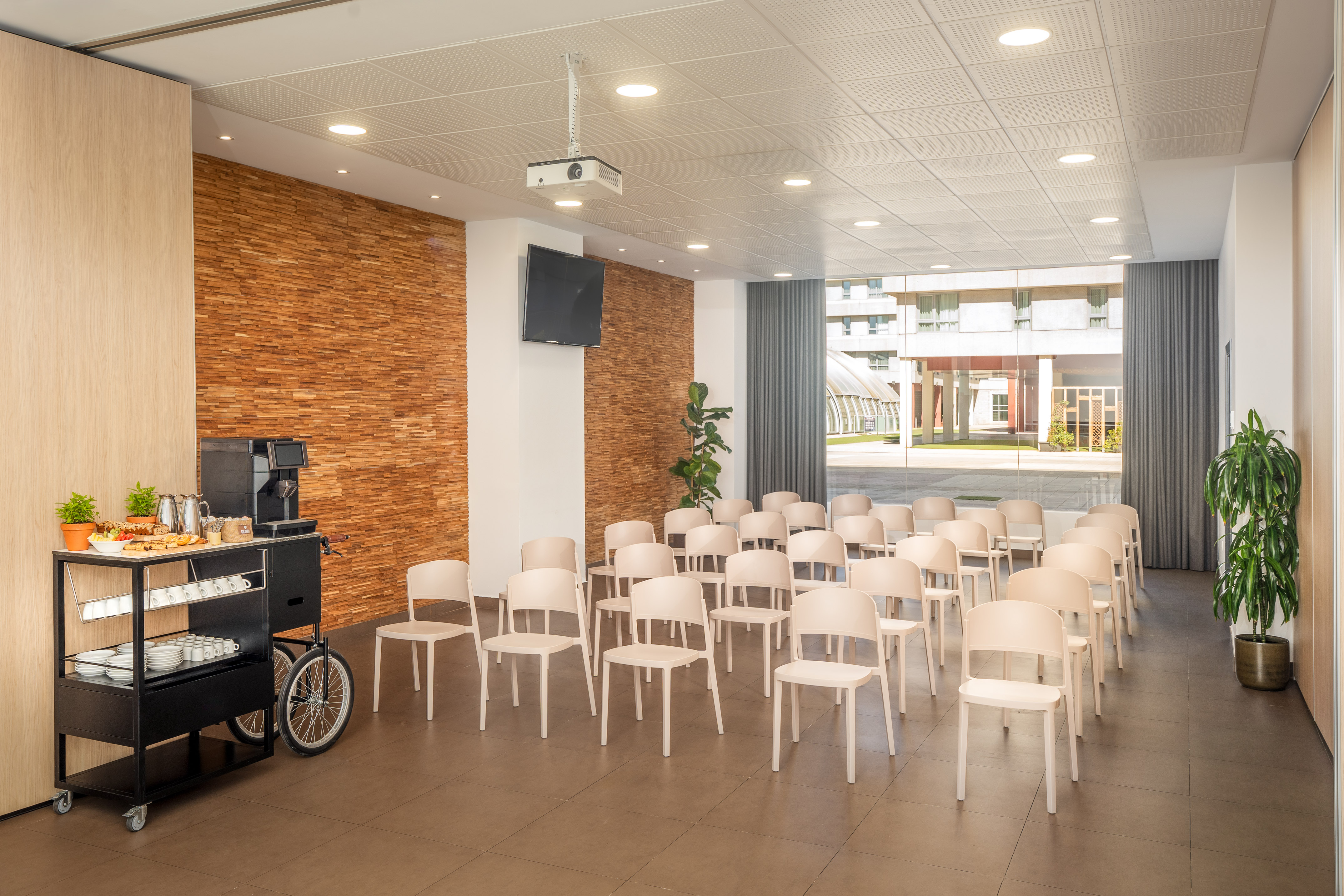 Modern conference room with beige chairs, projector, TV, and coffee break station.