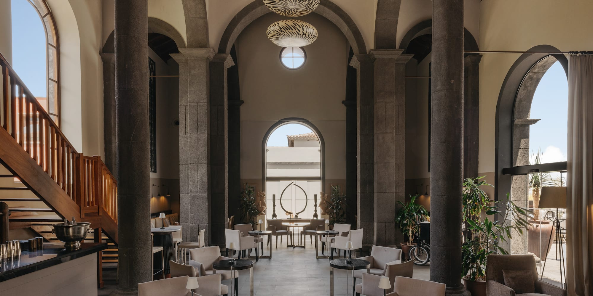 Elegant lounge with stone columns, arched windows, stylish seating, bar.