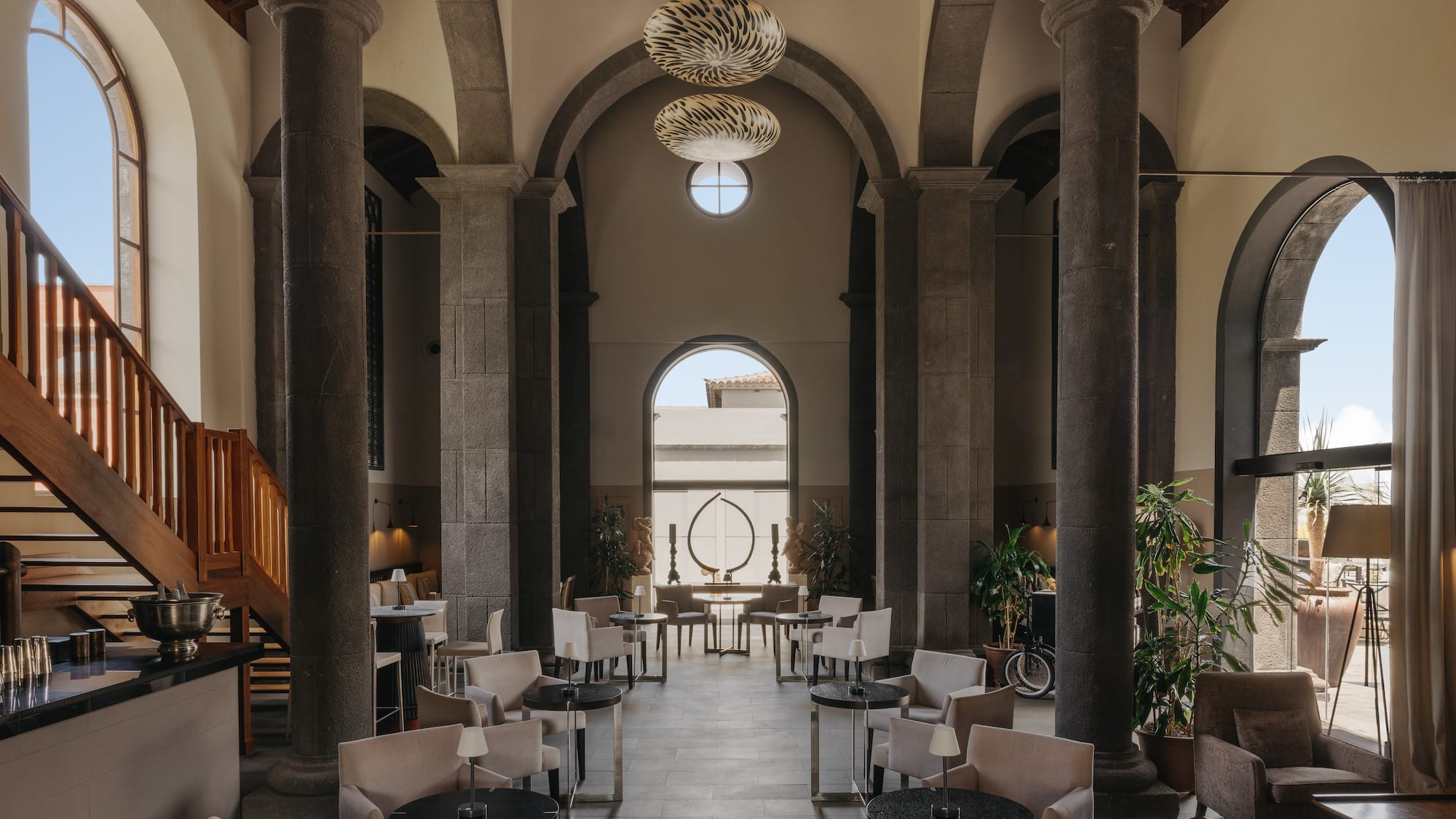 Elegant lounge with stone columns, arched windows, stylish seating, bar.